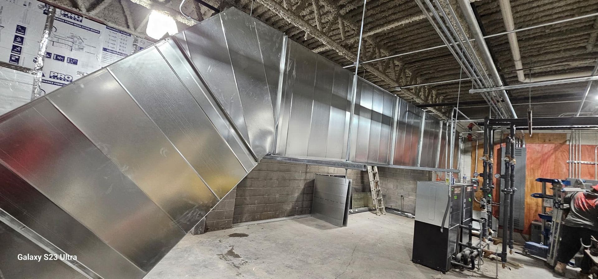 Large, metallic HVAC ductwork installation in an industrial interior.