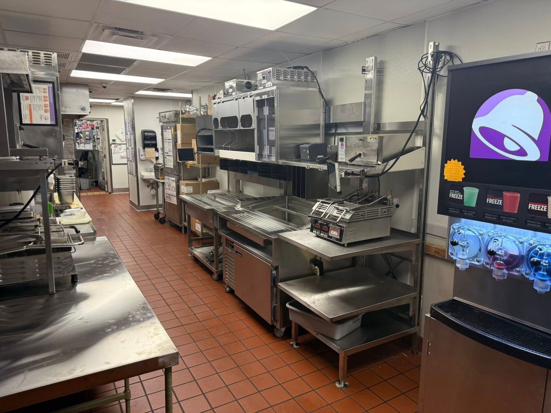 A Taco Bell kitchen with stainless steel equipment and a drink dispenser.
