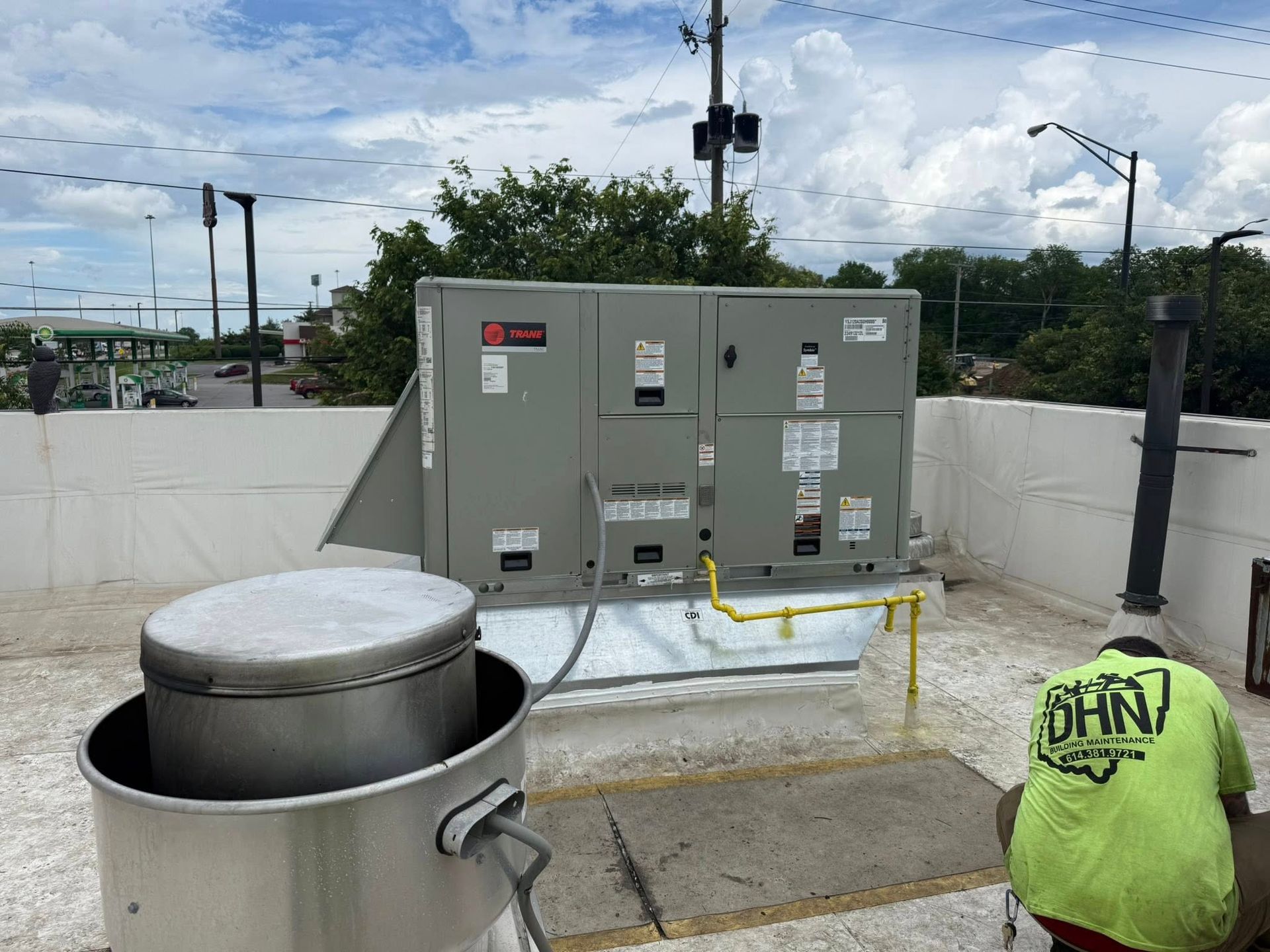 Rooftop HVAC unit next to a vent, a worker in safety gear, and a cloudy sky.