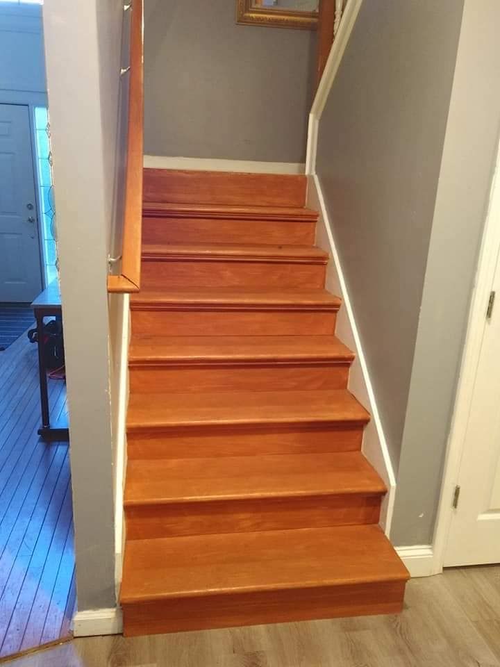 Wooden staircase with tan steps, gray walls, and white trim.