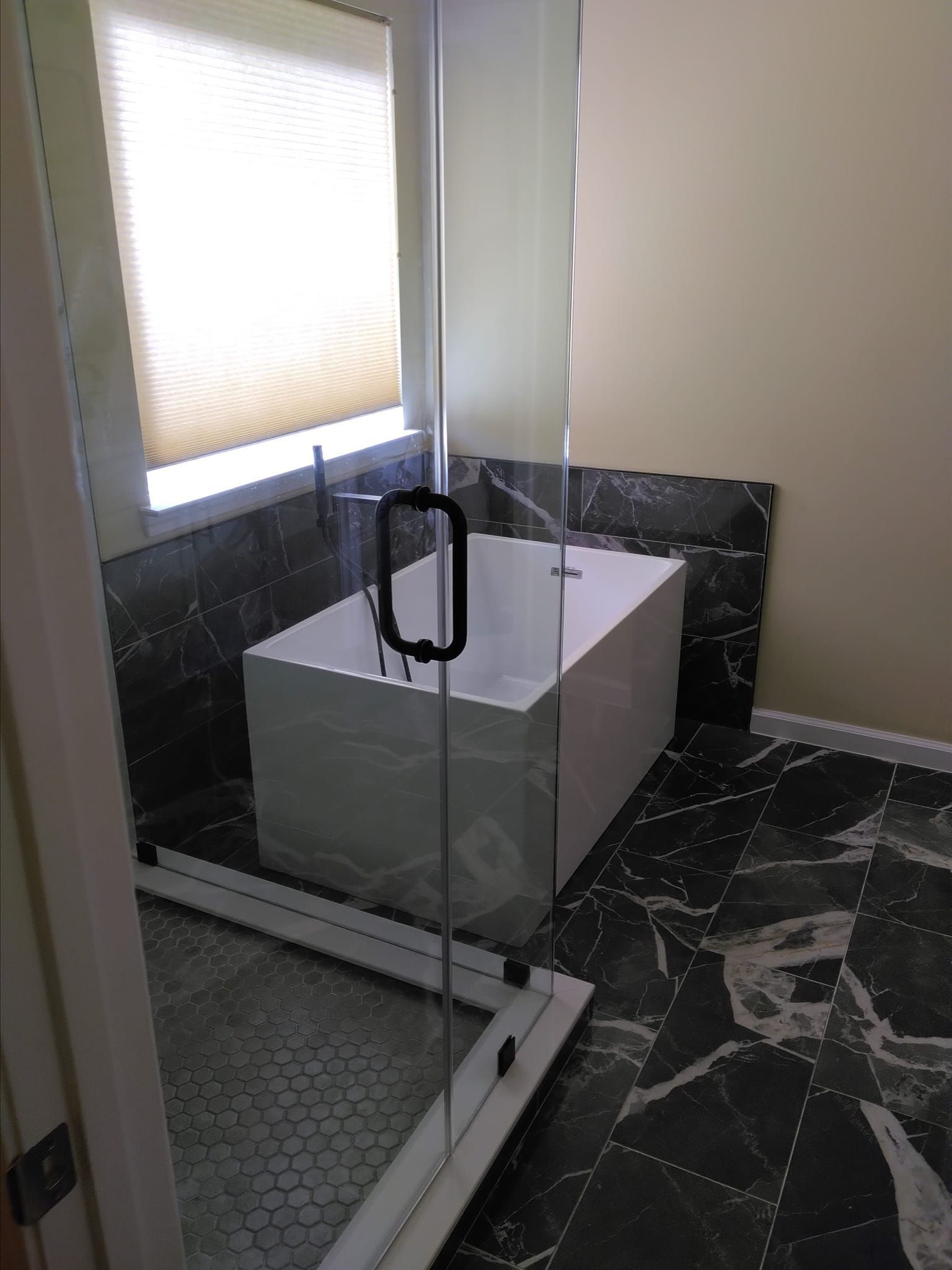 Modern bathroom with white rectangular tub, black and white marble tile, and a glass shower door.