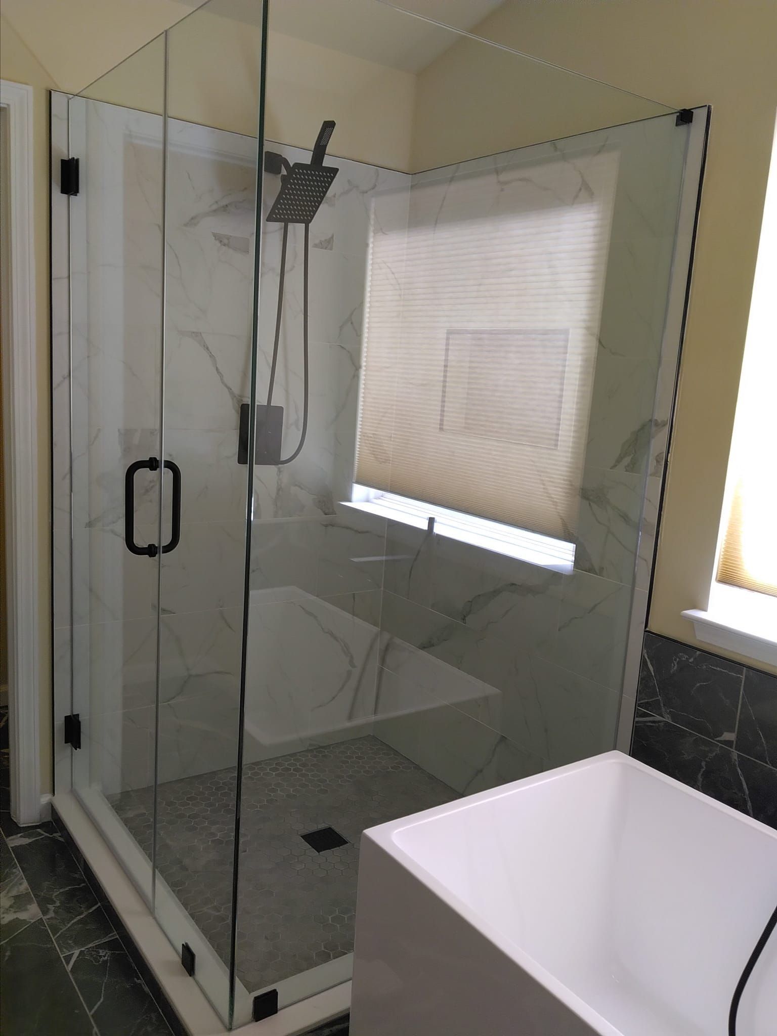Corner glass shower with marble tile, black hardware, and rain shower head.
