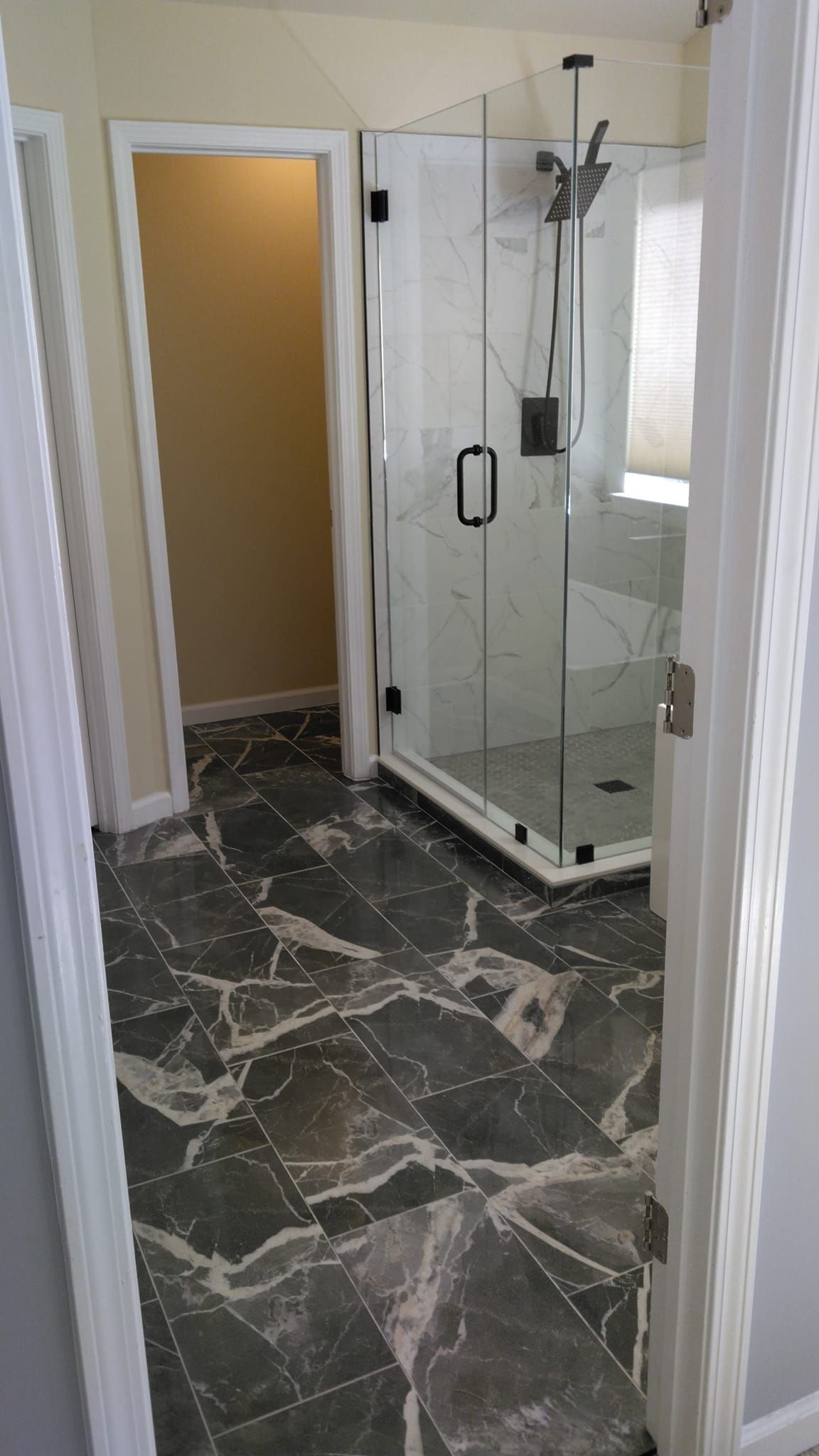 Bathroom with dark marble tile floor, glass shower, and doorway leading to a room with light yellow walls.