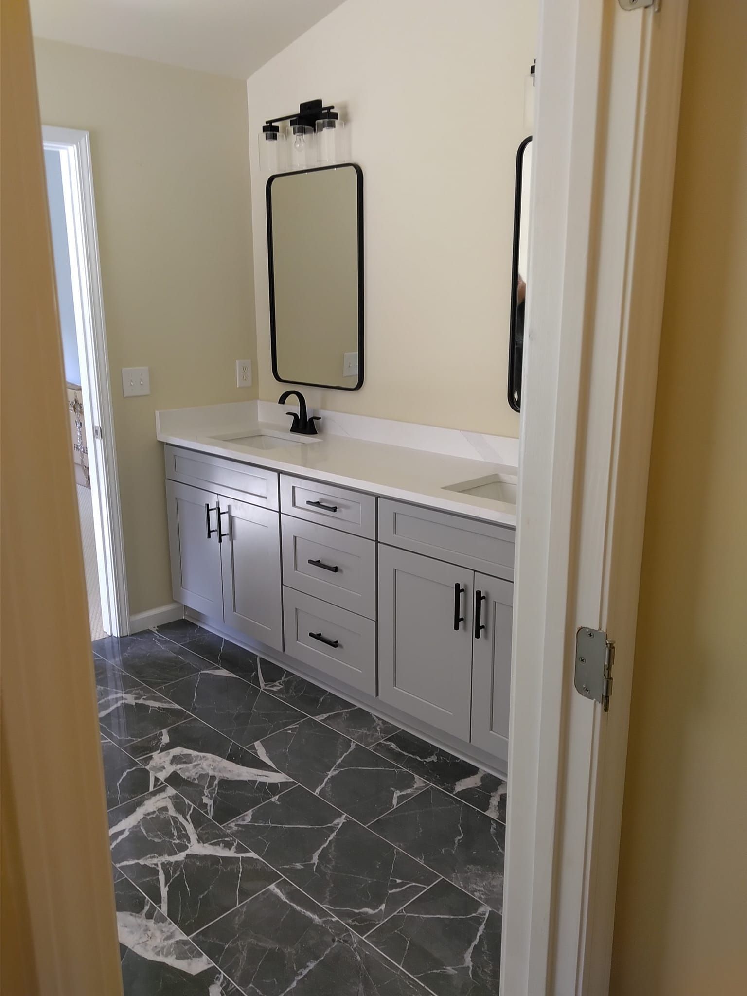 Bathroom with gray cabinets, white countertop, black fixtures, and patterned tile floor.