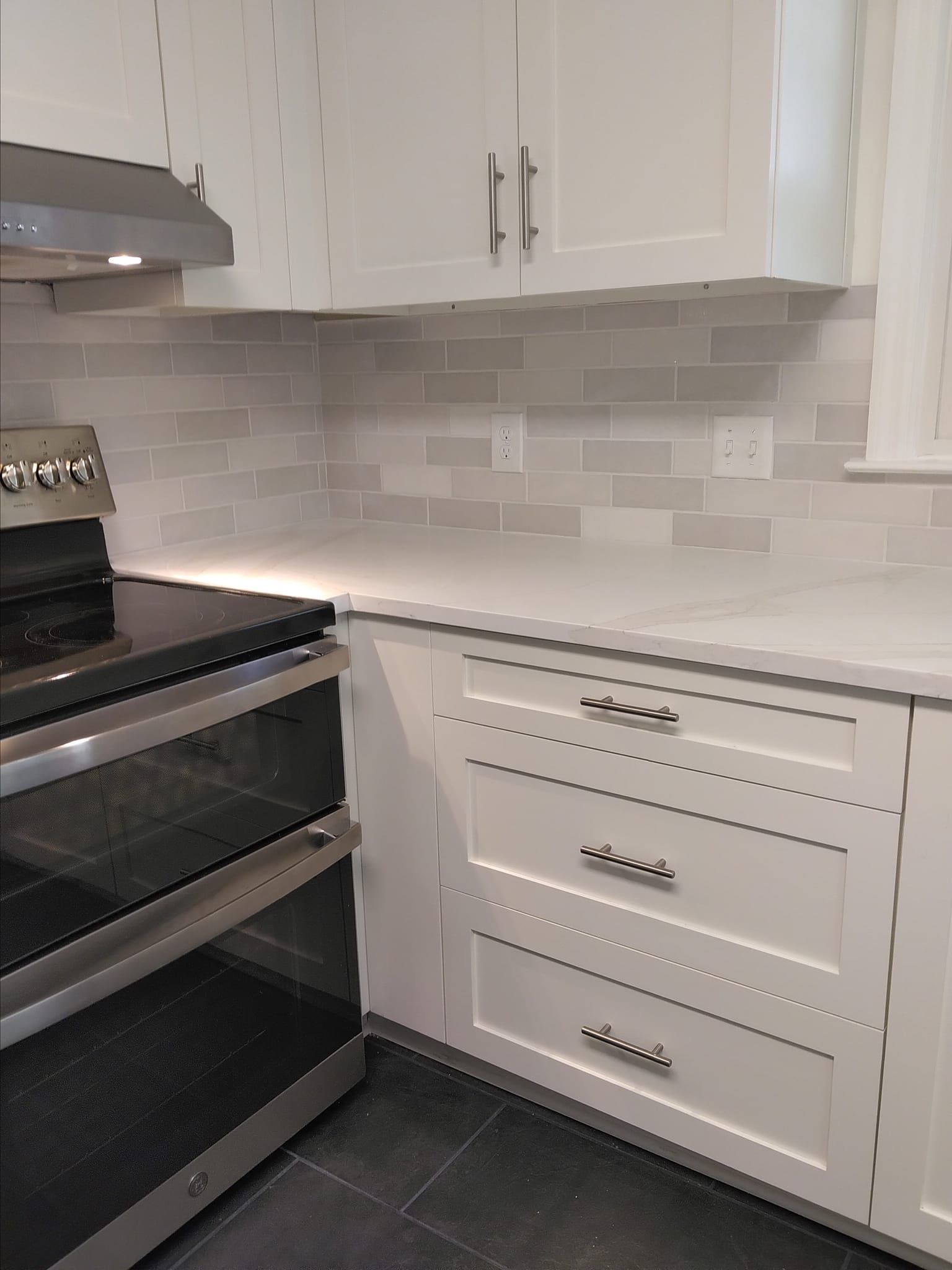 White kitchen corner with oven, cabinets, and light gray backsplash.