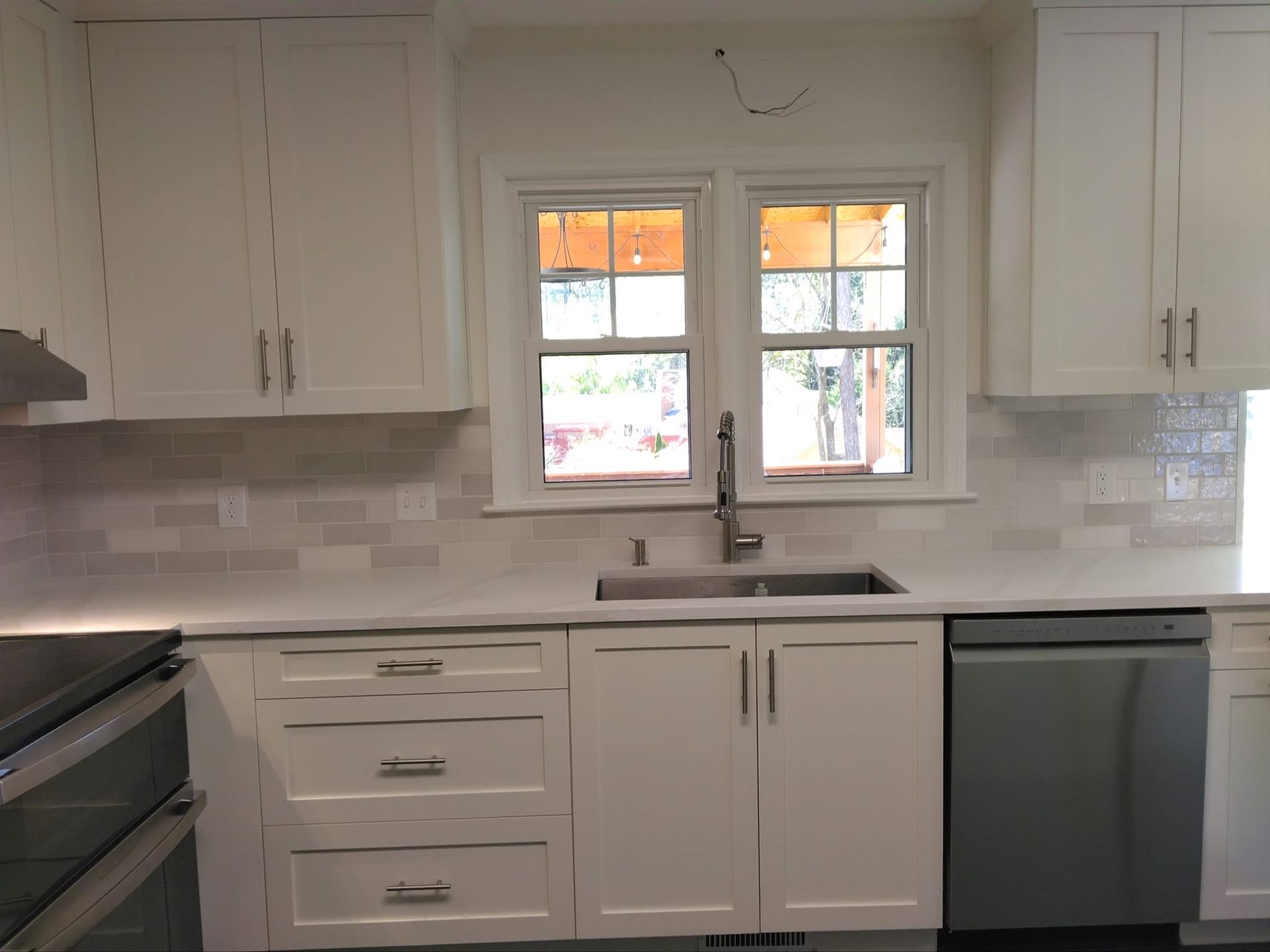 White kitchen cabinets and counters, subway tile backsplash, sink under a window.