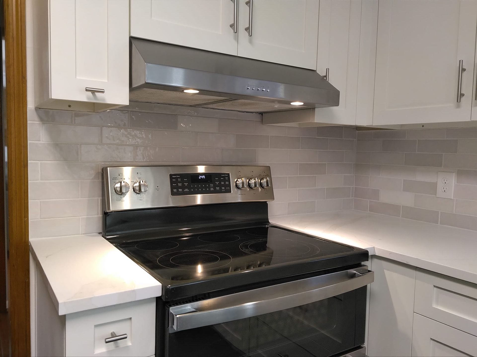 Kitchen with white cabinets, stainless steel range and hood, light gray backsplash.