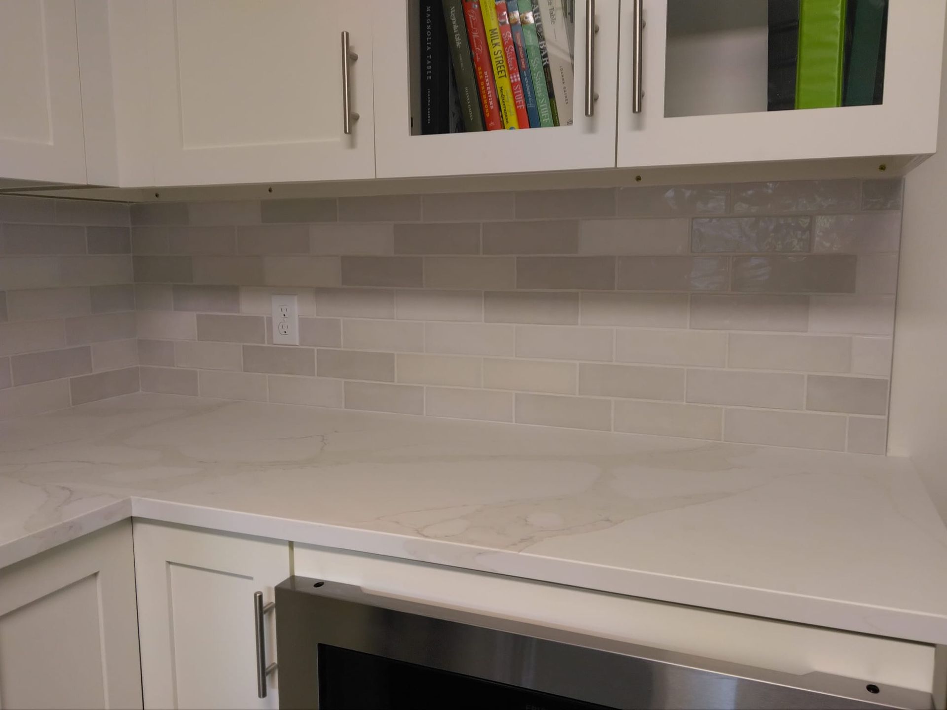 White kitchen countertop with light gray tiled backsplash and cabinets.