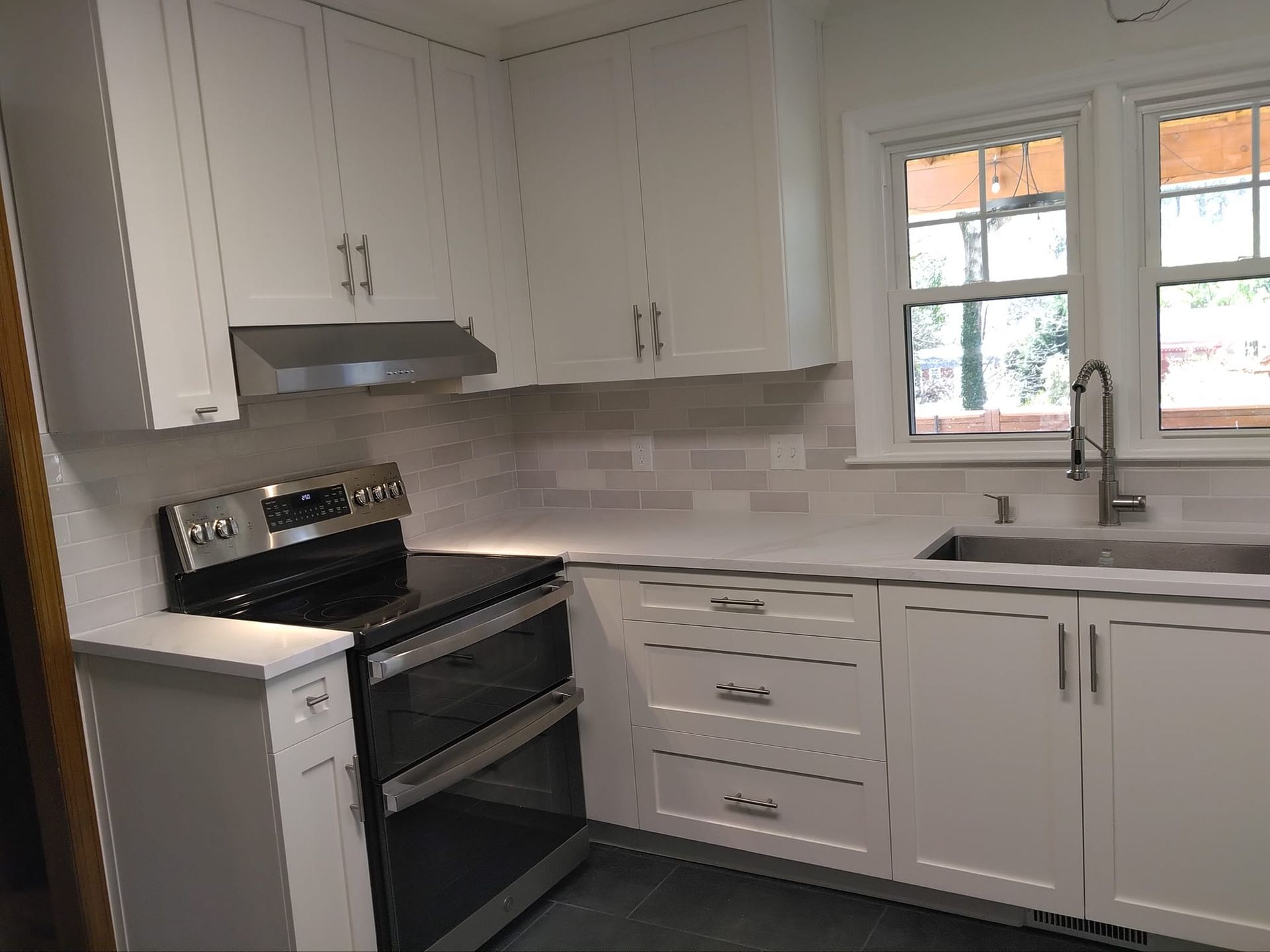 White kitchen with oven, cabinets, sink, and window.
