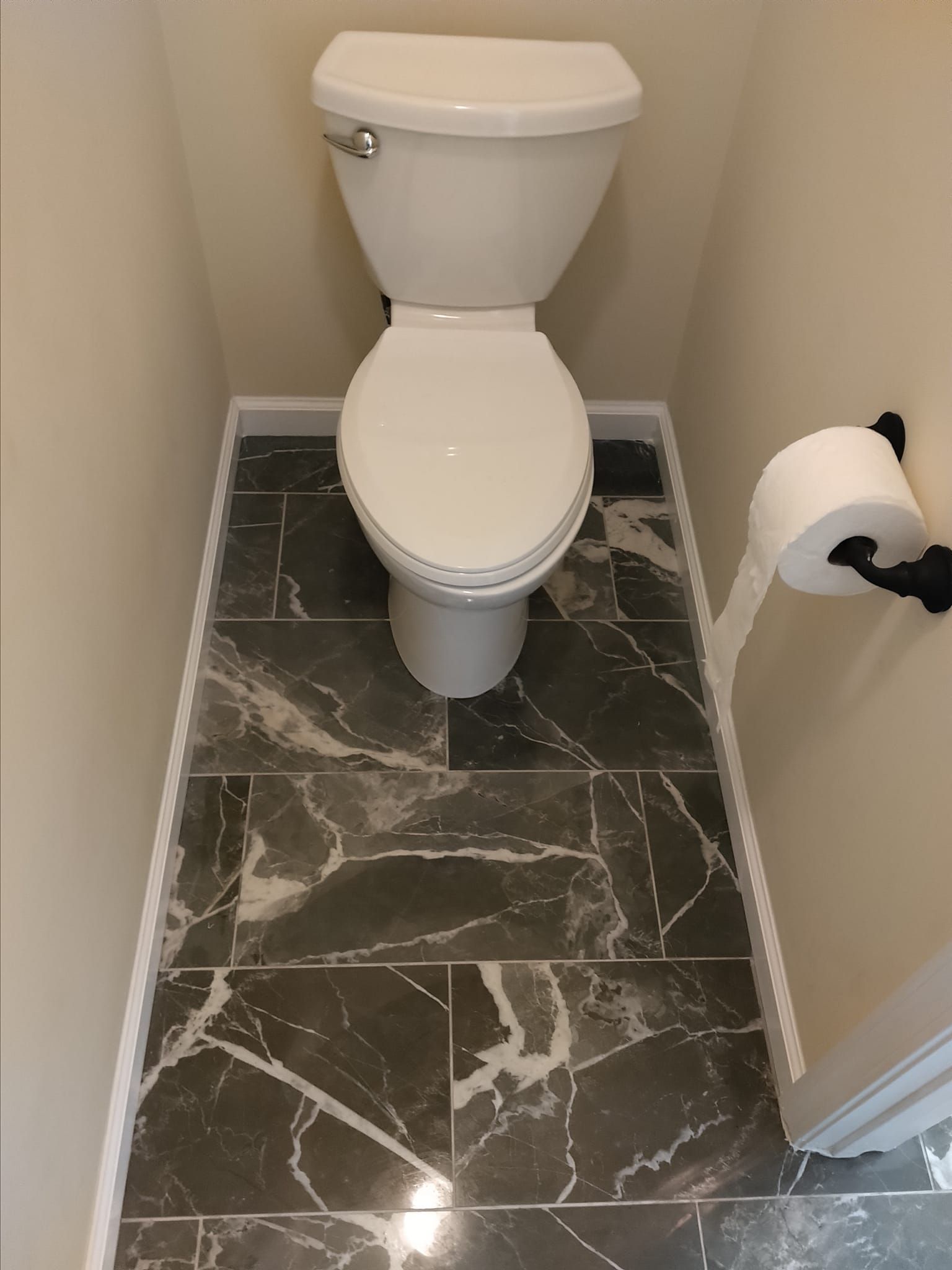 Toilet in a small bathroom with dark gray marble-look tile floor and a roll of toilet paper on the right.