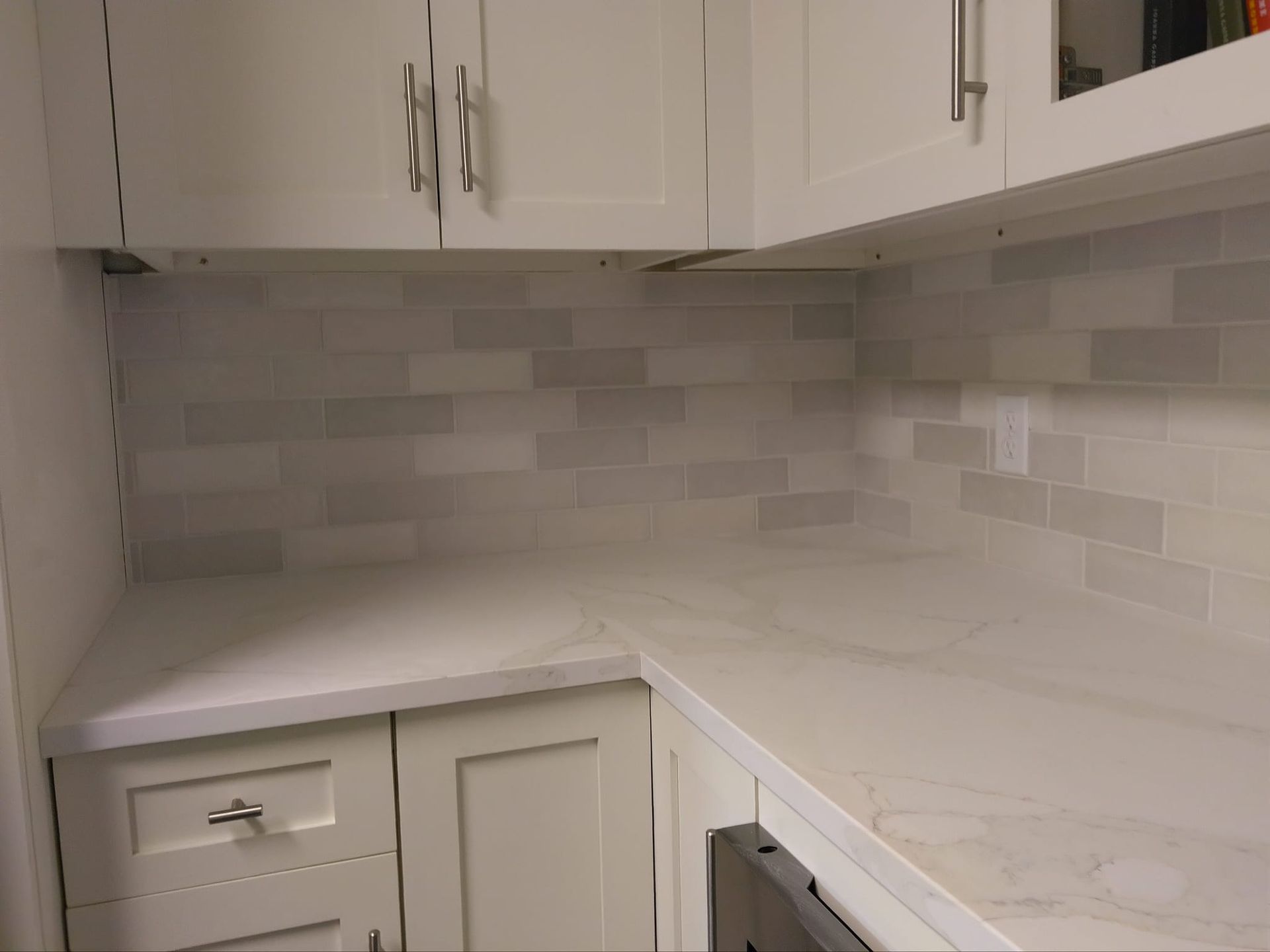 White kitchen cabinets and countertops with a grey tiled backsplash.