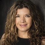 A woman with curly hair is smiling and wearing a black shirt.