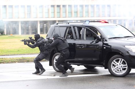 A group of soldiers are running towards a police car.