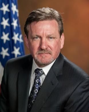 A man in a suit and tie is standing in front of an american flag.