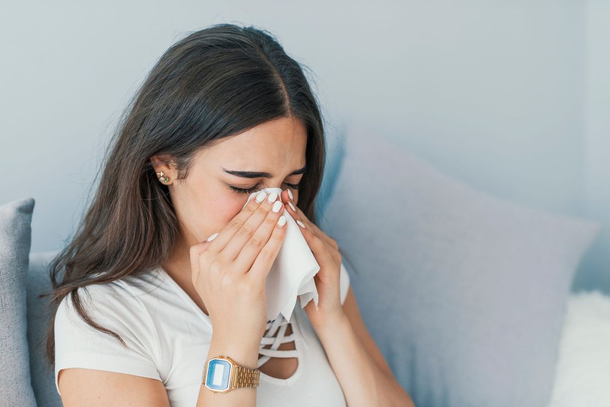 A woman is blowing her nose into a napkin while sitting on a couch.