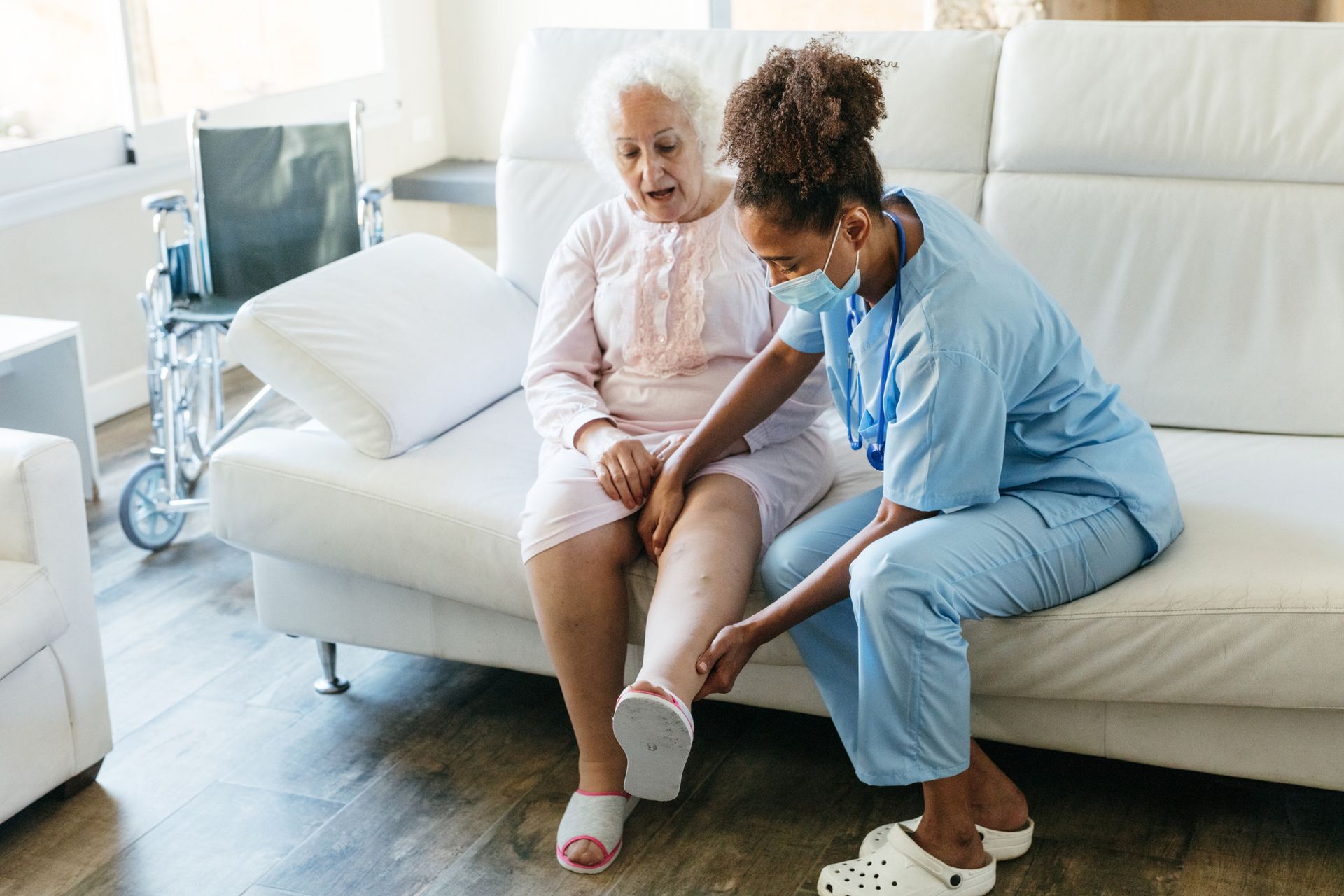 Nurse checks elderly woman's leg at varicose vein treatment center in senior care home.