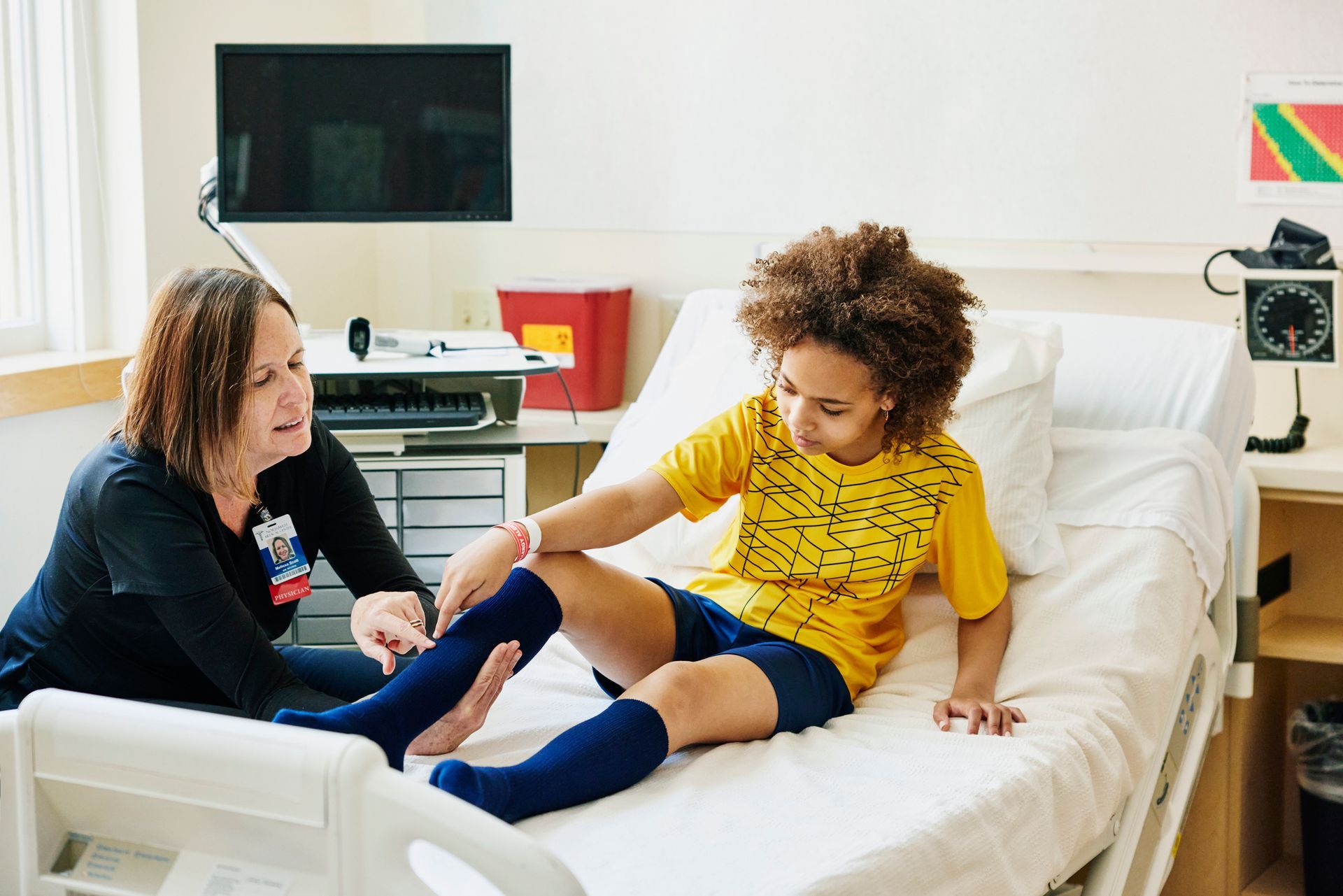 A doctor examining a young soccer player for a leg injury in an urgent care room.