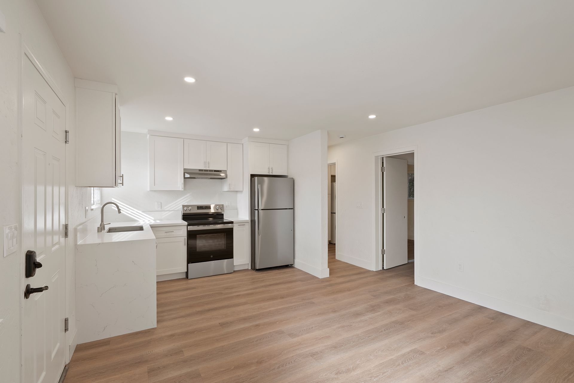Bright, minimalist kitchen with white cabinets, stainless steel appliances, and wood-look flooring.