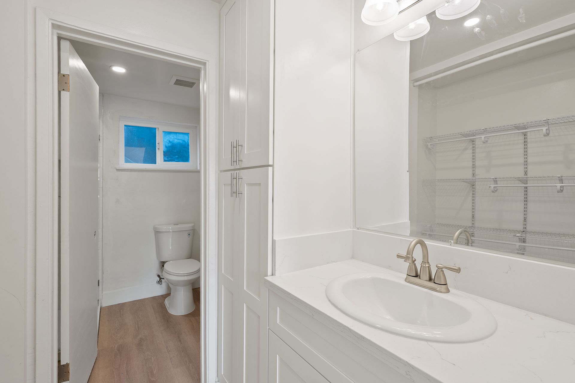 White bathroom with a sink, mirror, and toilet visible through an open door.