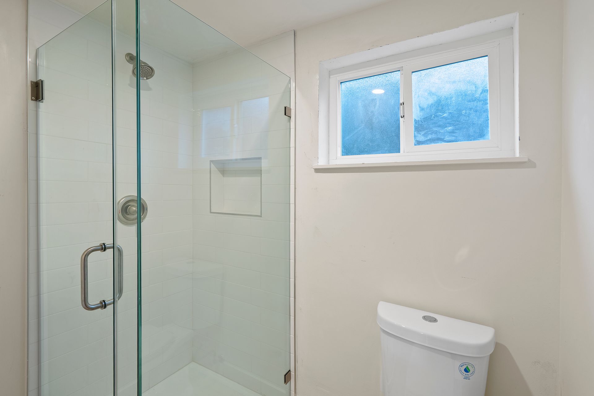 Bathroom with glass shower, toilet, and window with frosted glass.