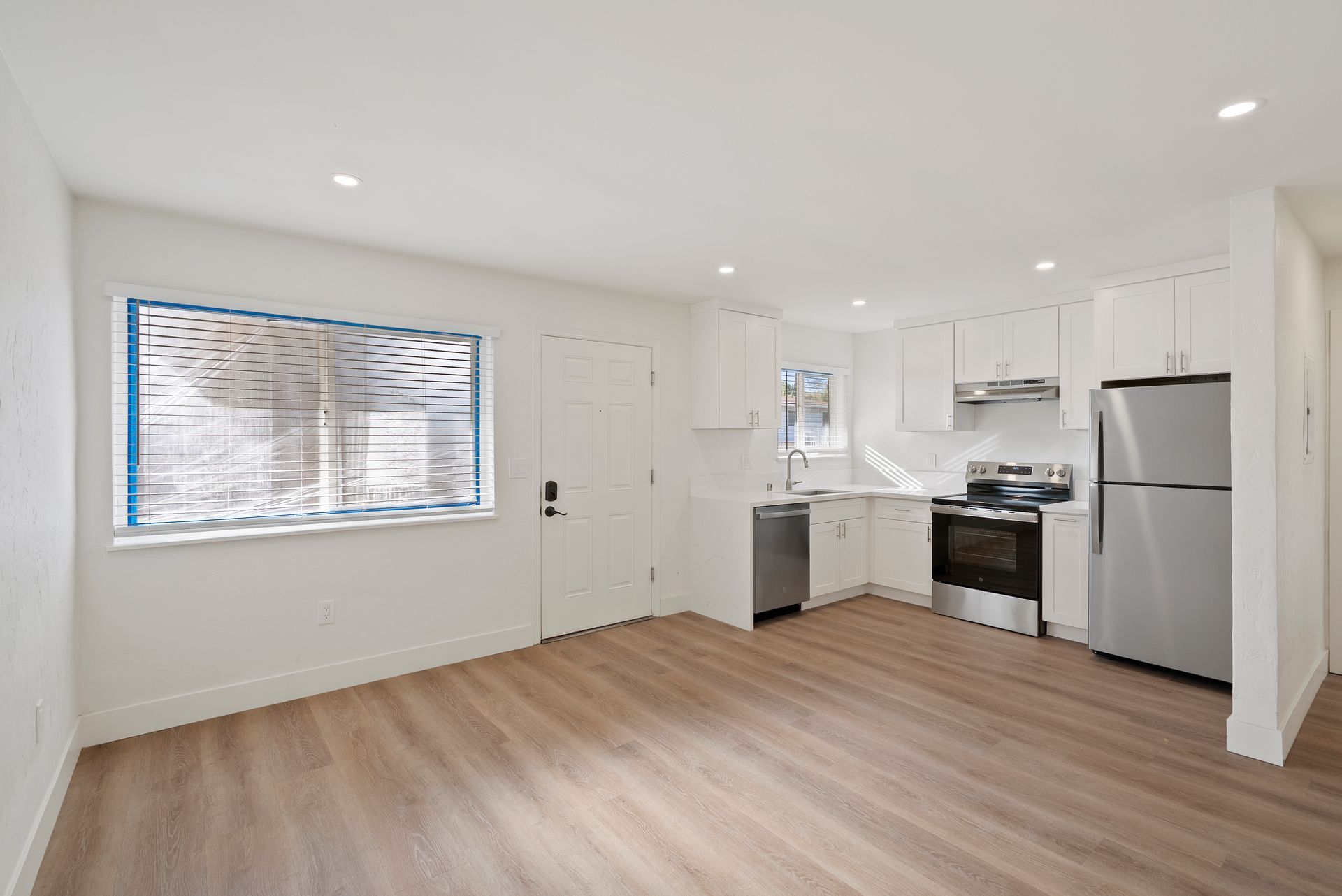 Empty, bright apartment interior with a kitchen, window, and stainless steel appliances.
