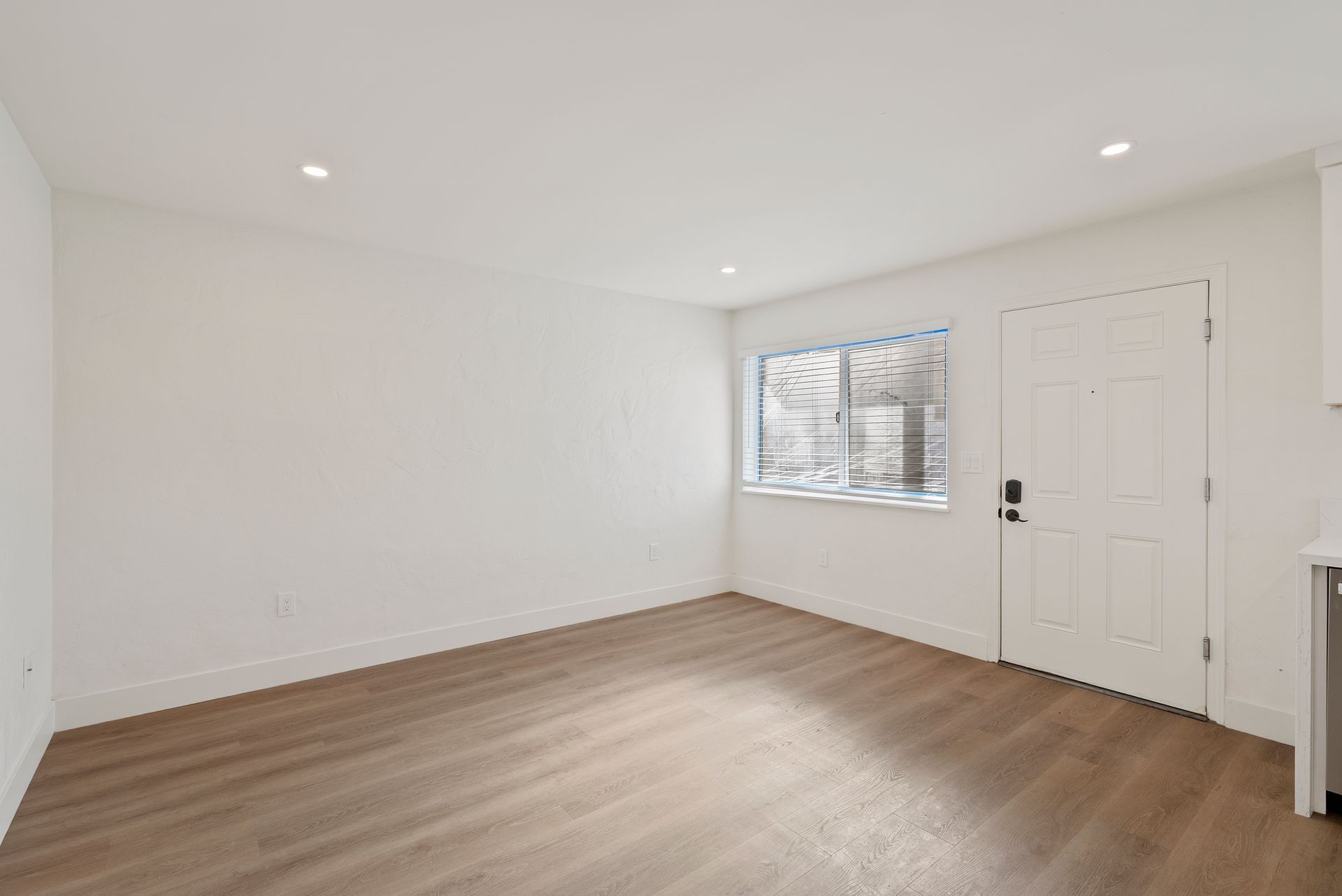 Empty room with wood-look flooring, white walls, a window, and a door.