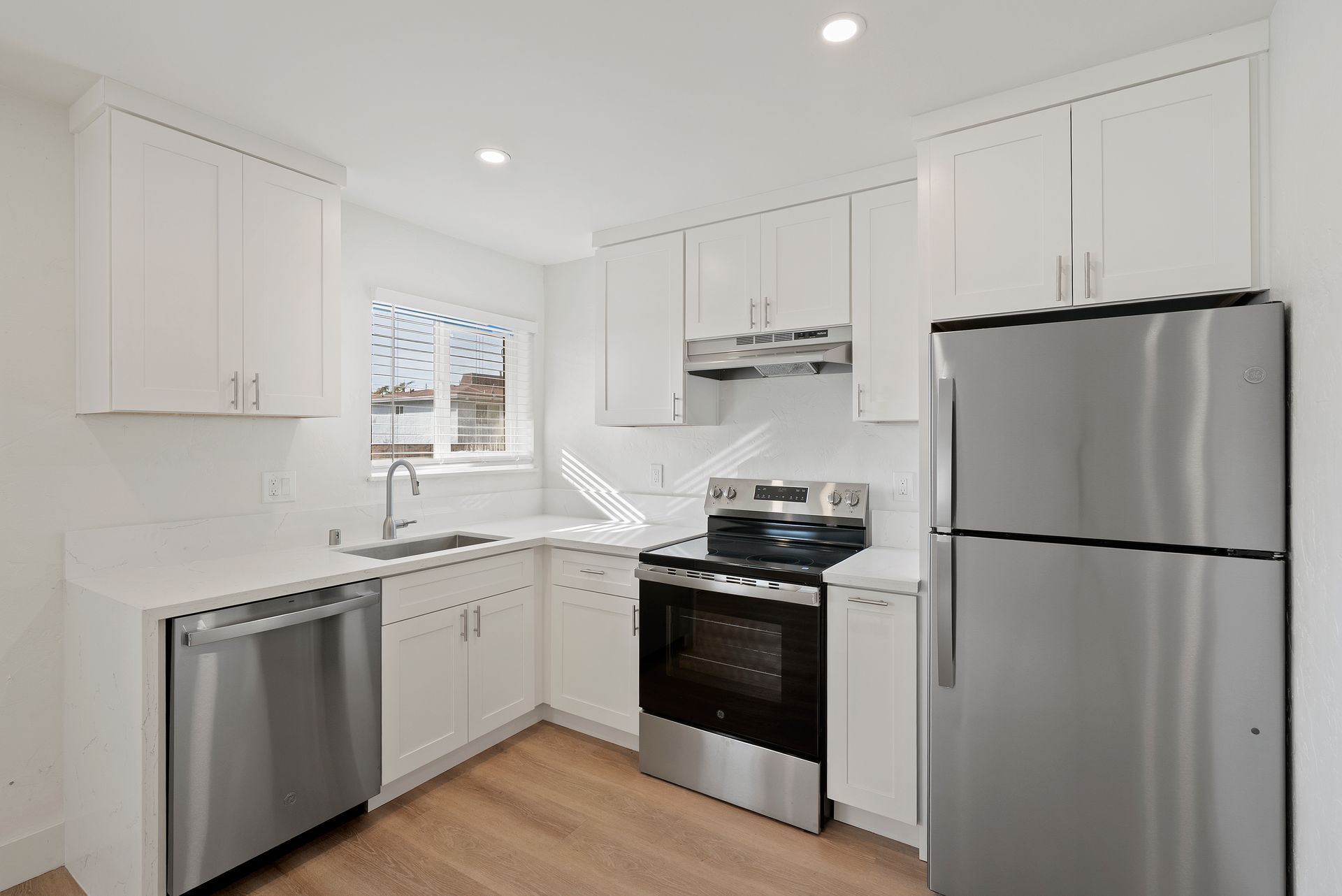White kitchen with stainless steel appliances, cabinets, and light wood floors.