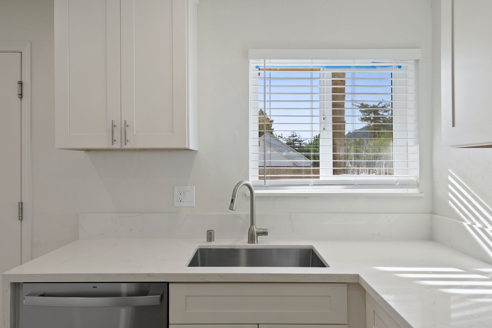 White kitchen with sink under a window, cabinets, and countertop.