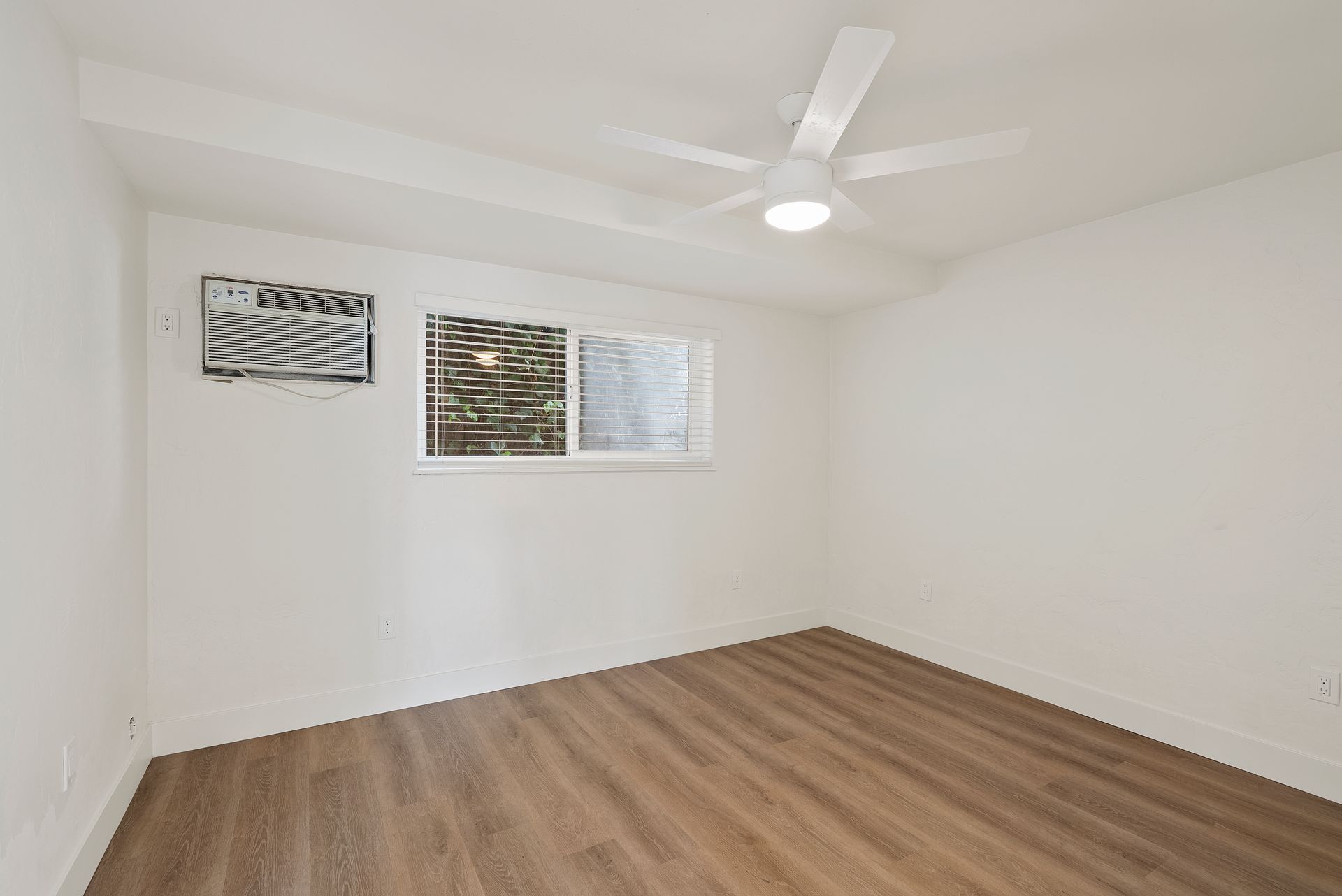 Empty bedroom with wood flooring, white walls, ceiling fan, and window.
