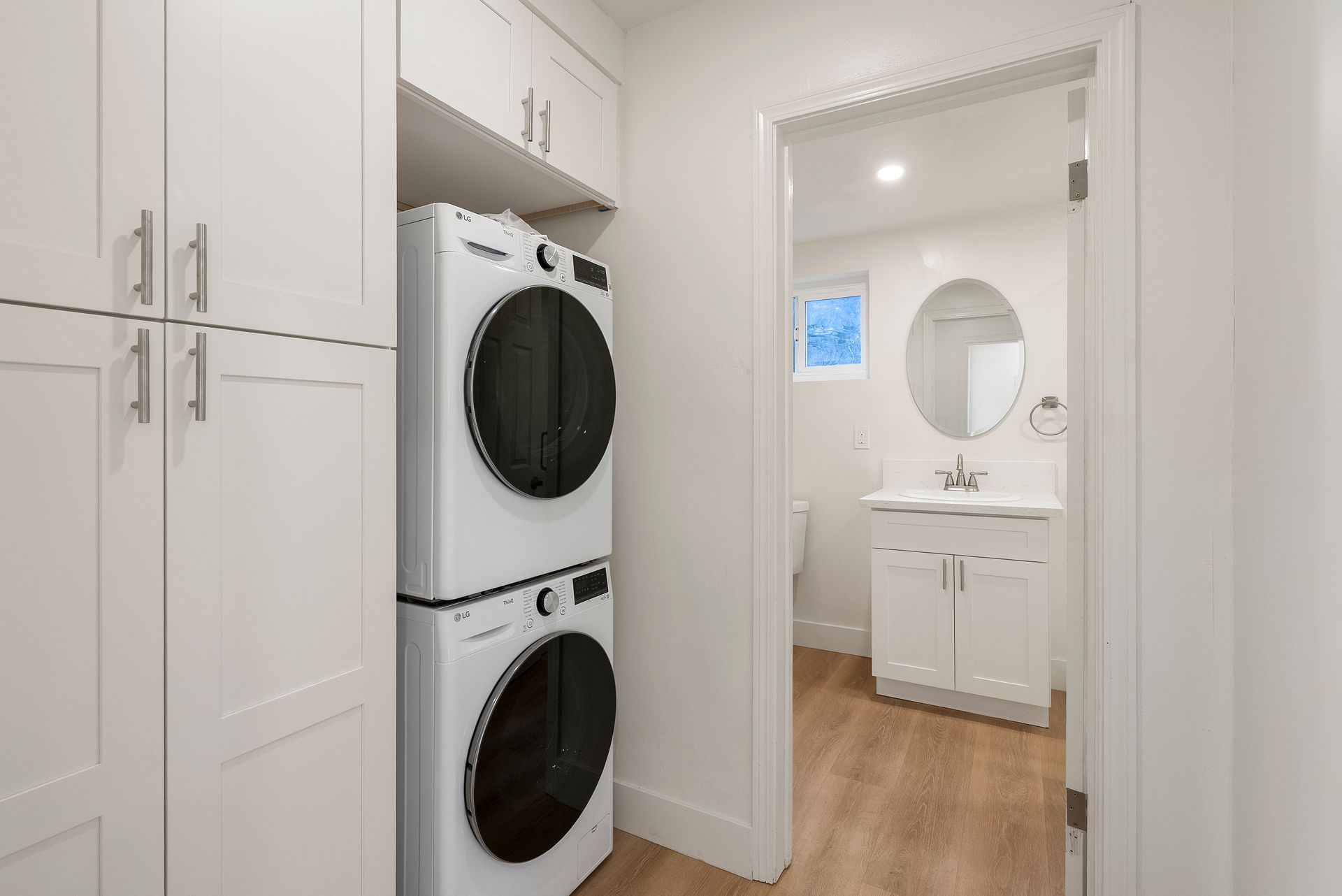 Laundry room with stacked white washer/dryer, white cabinets, and doorway to a bathroom.