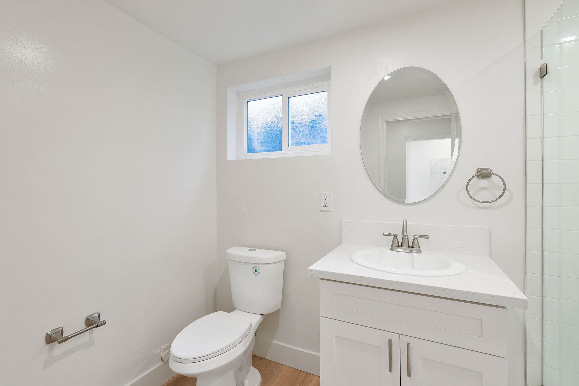 White bathroom with toilet, sink, mirror, and small window.