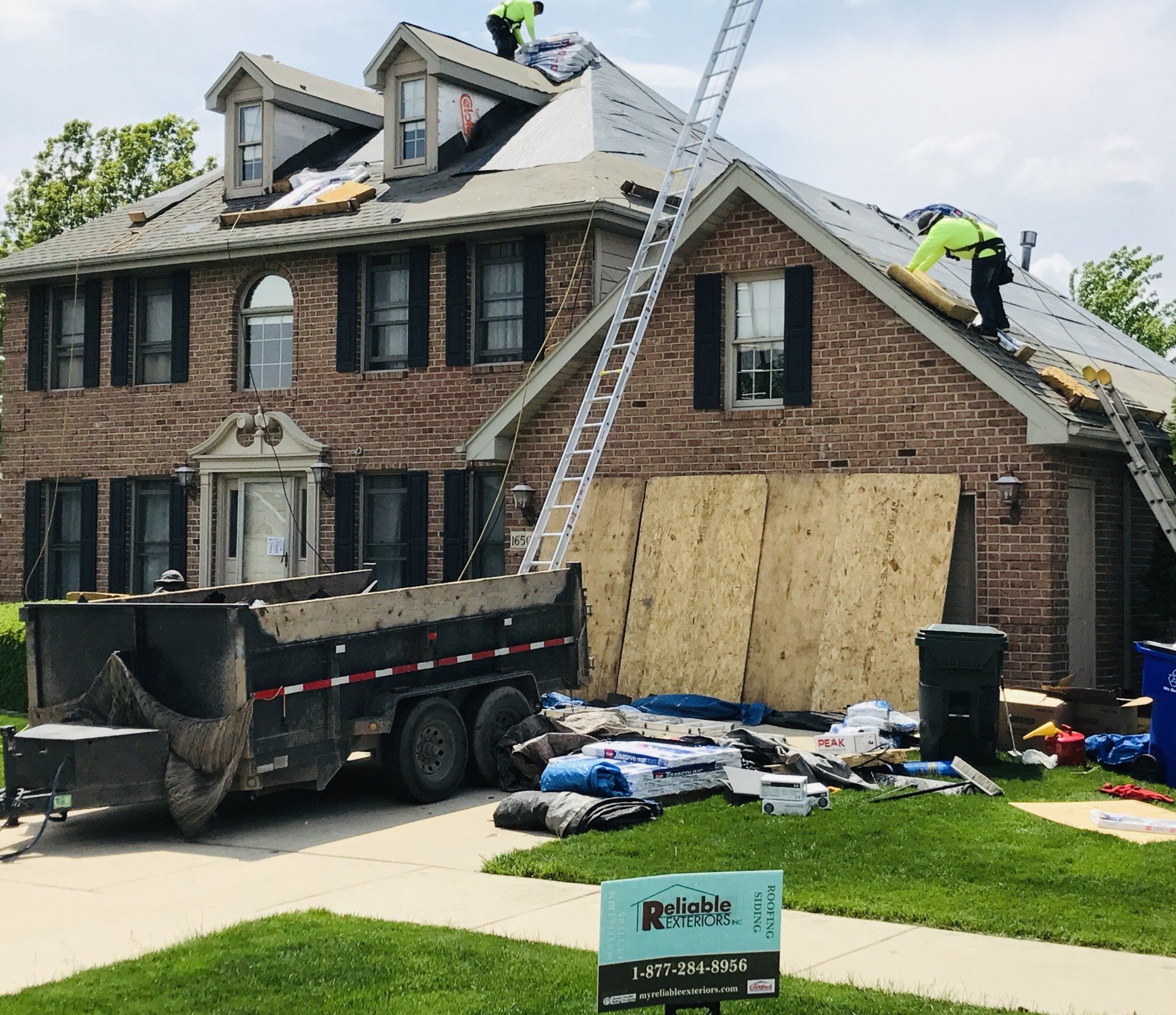 A brick house with a dumpster in front of it and workers on the roof.