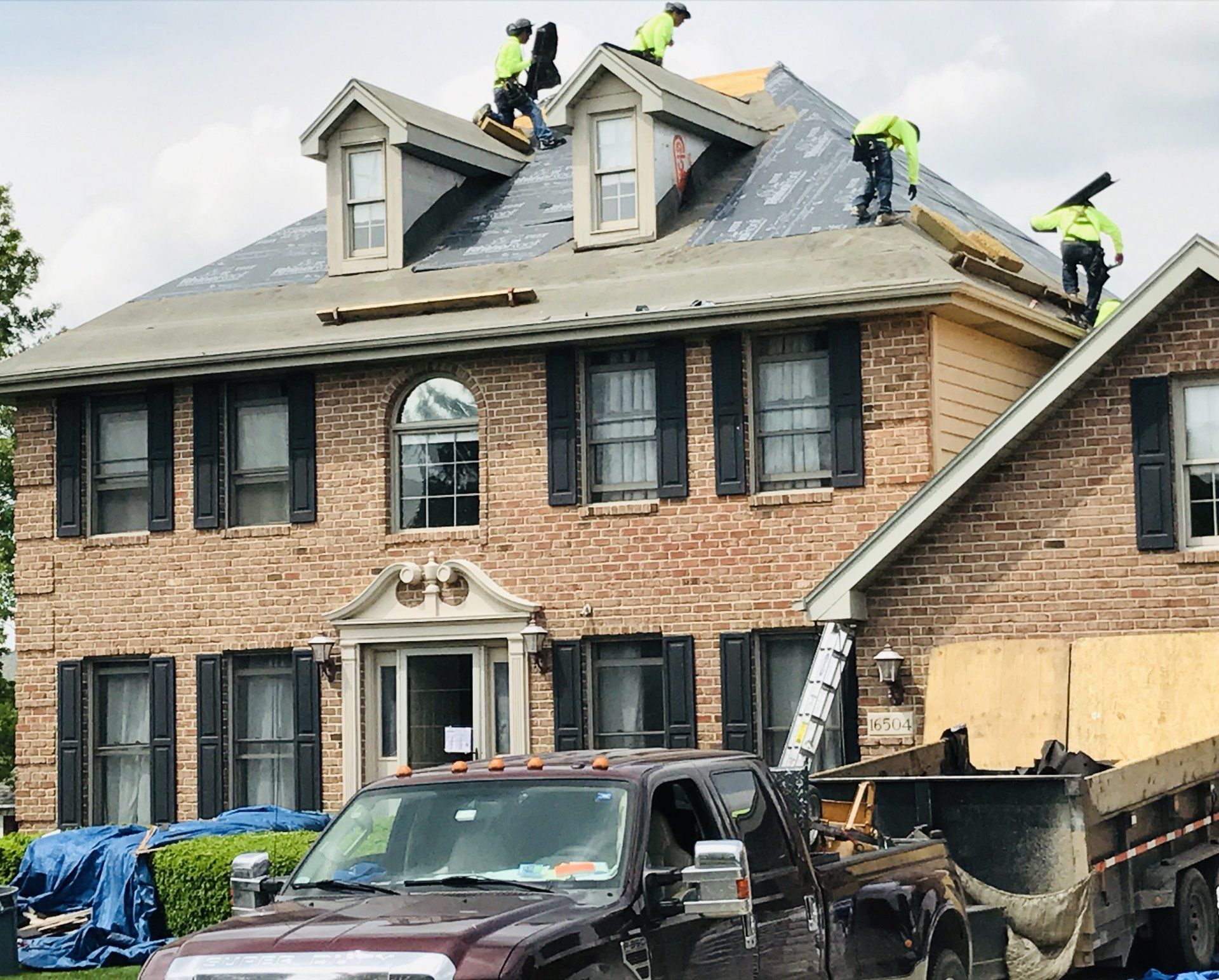 A group of men are working on the roof of a large brick house.