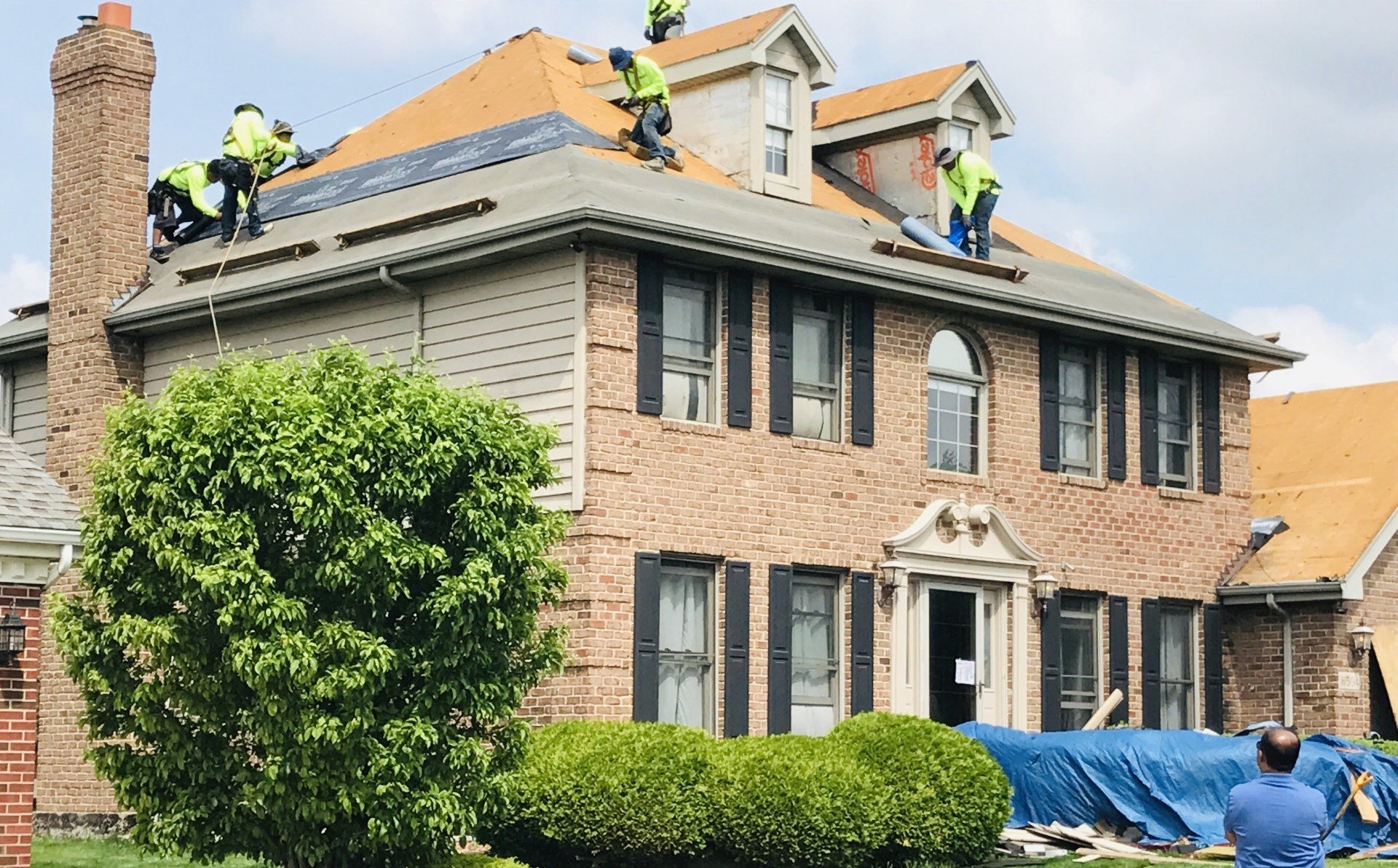 A group of men are working on the roof of a large brick house.