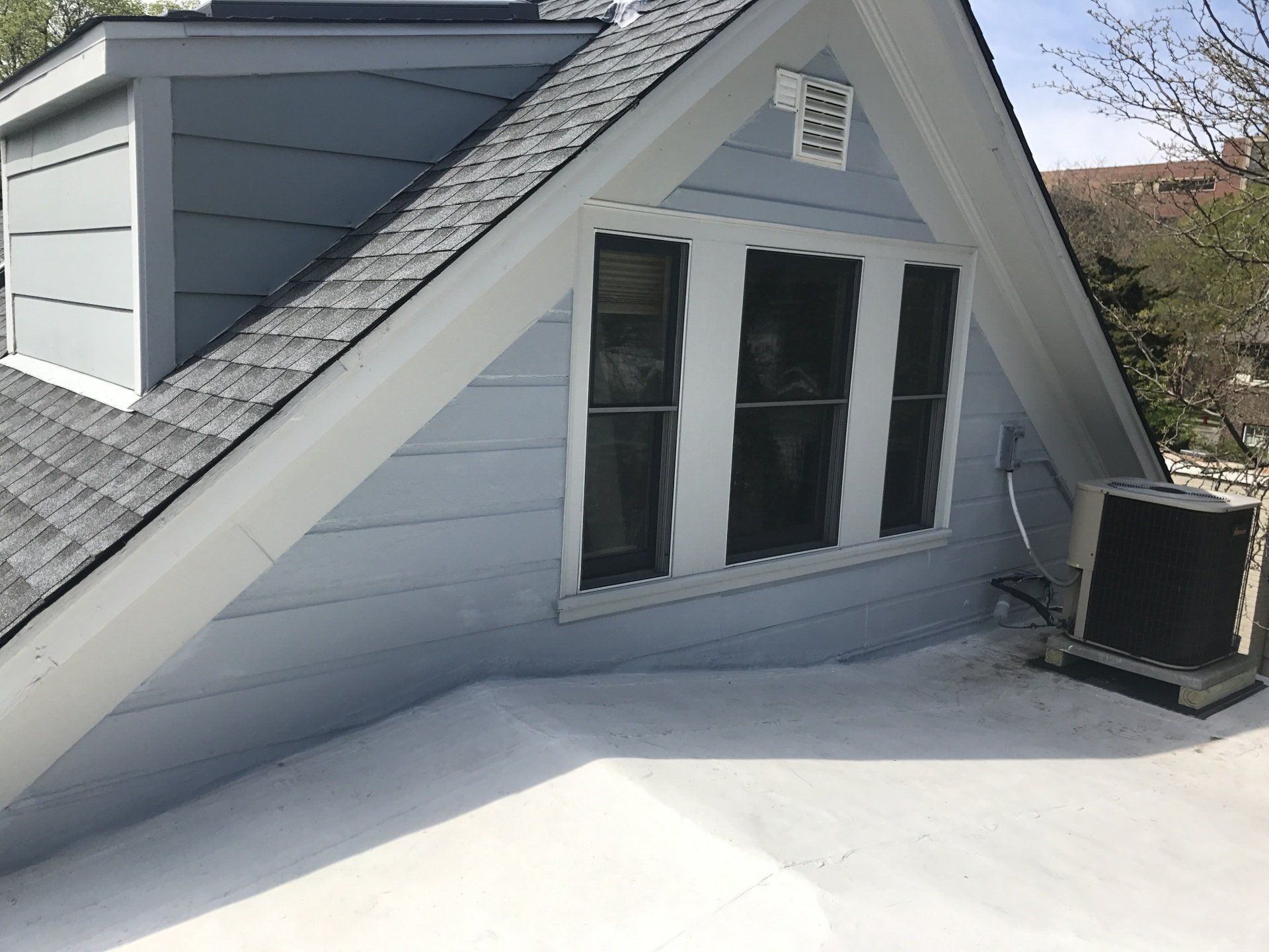 The roof of a house with a window and a fan on it.
