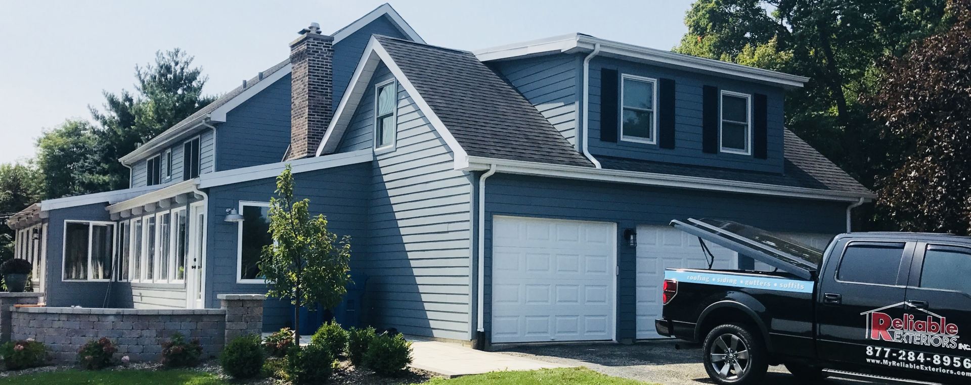 A black truck is parked in front of a blue house.