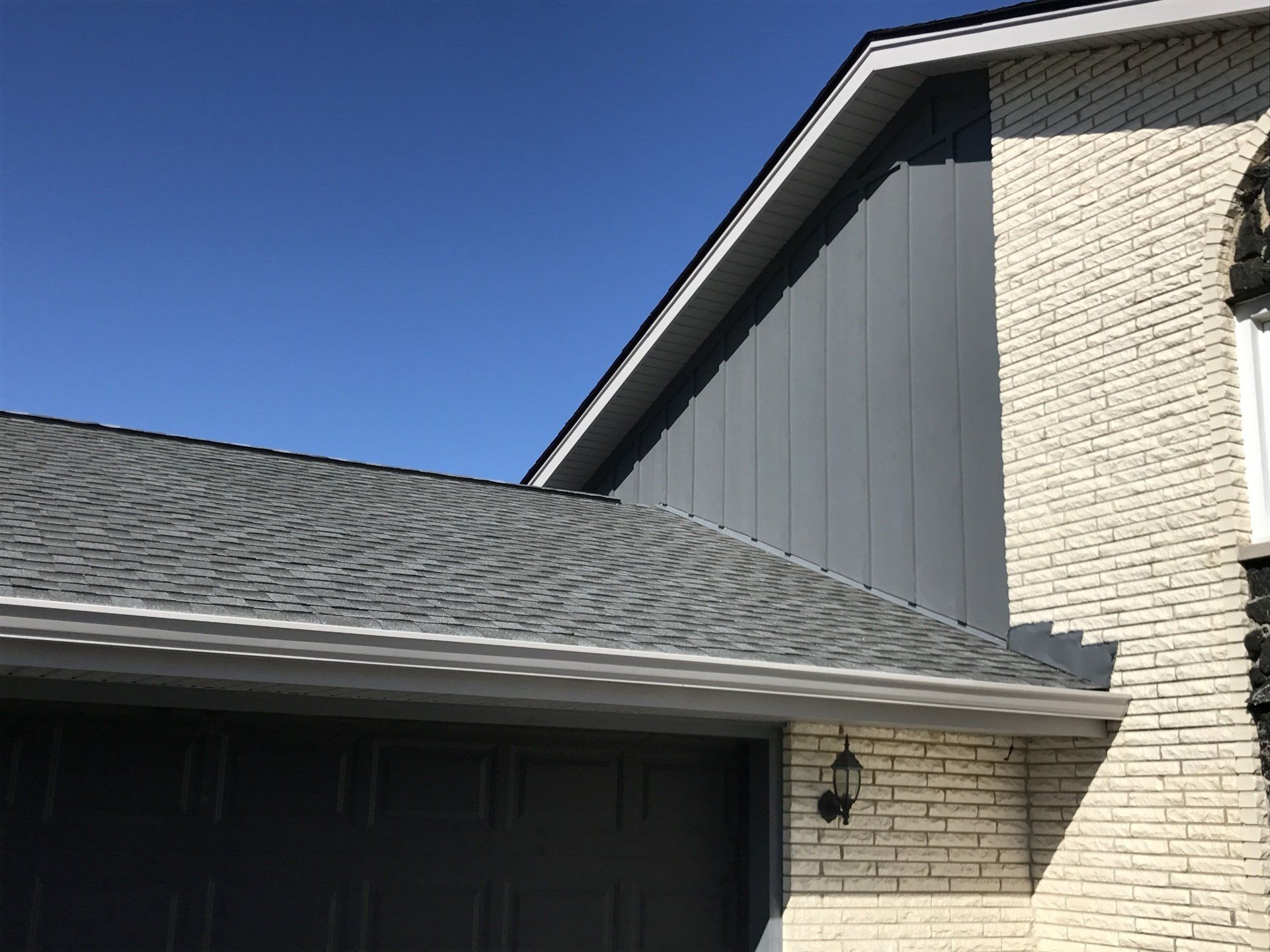 A white brick house with a gray roof and a black garage door