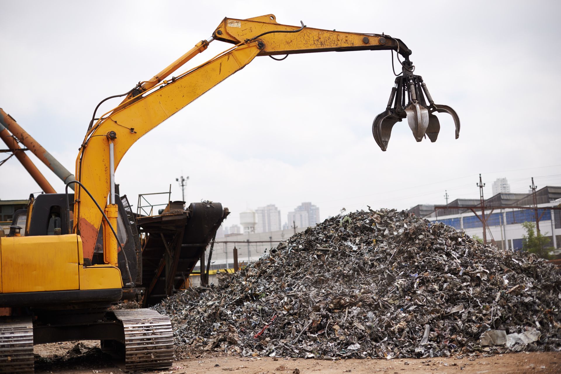A yellow excavator is working on a pile of scrap metal.