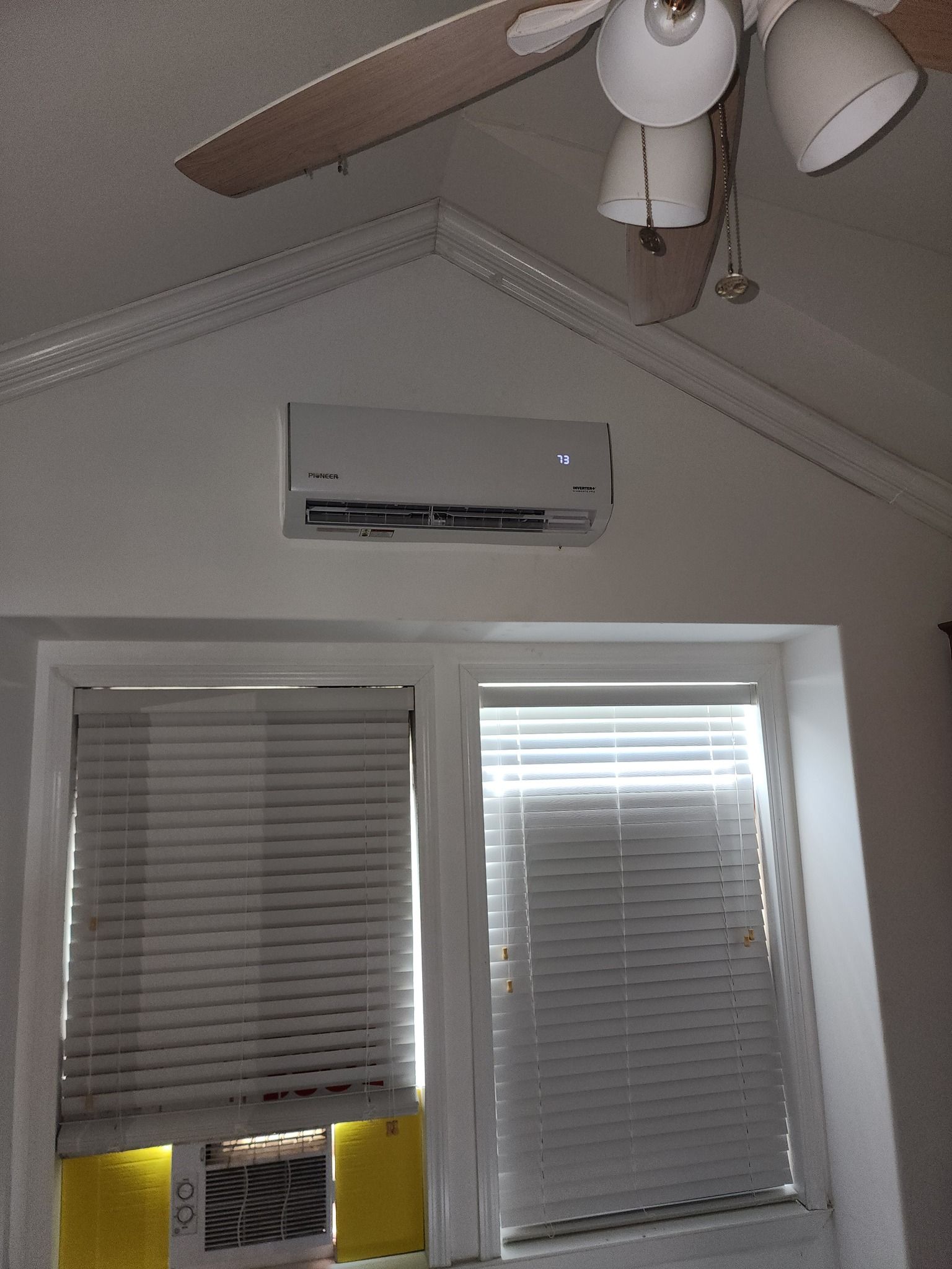 A white air conditioner is hanging from the ceiling above a window.