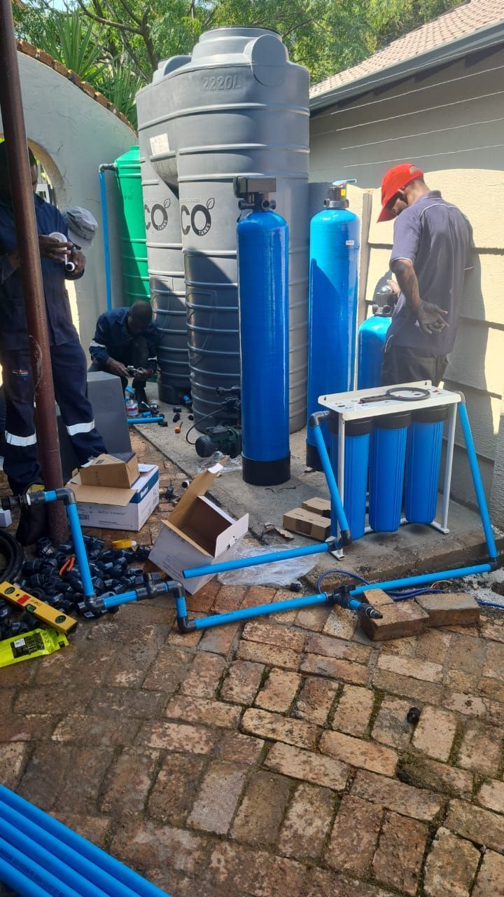 Workers installing water filtration system with blue pipes and tanks outside.