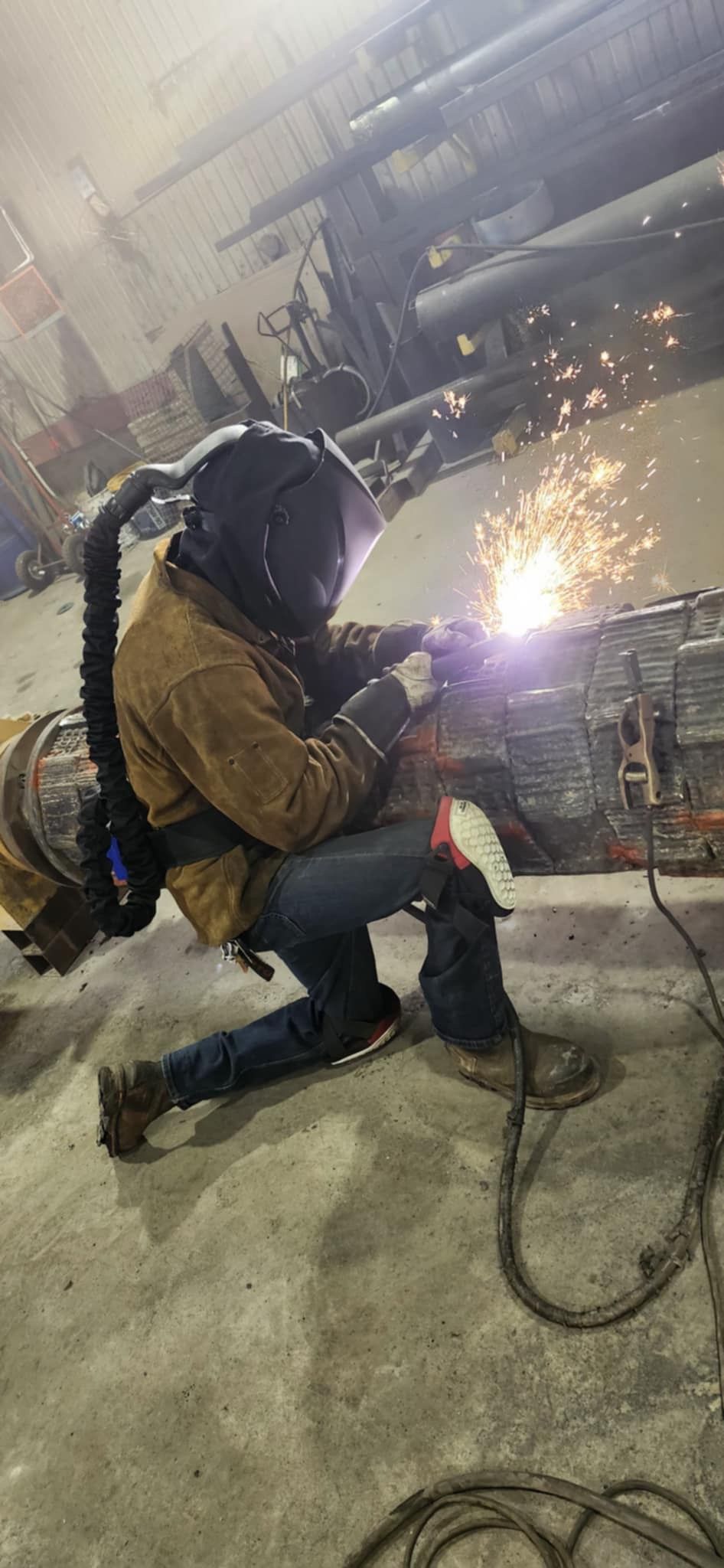 Un homme est à genoux et soude un morceau de métal dans une usine.