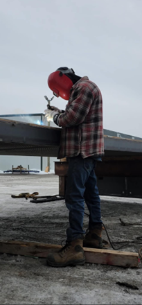Un homme en chemise à carreaux soude un morceau de métal.