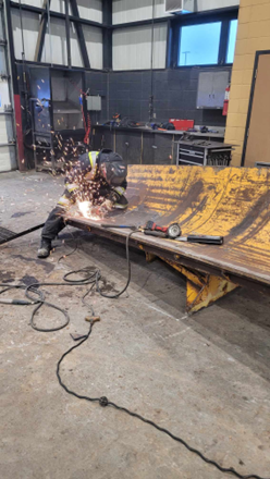 Un homme soude un morceau de métal dans un garage.