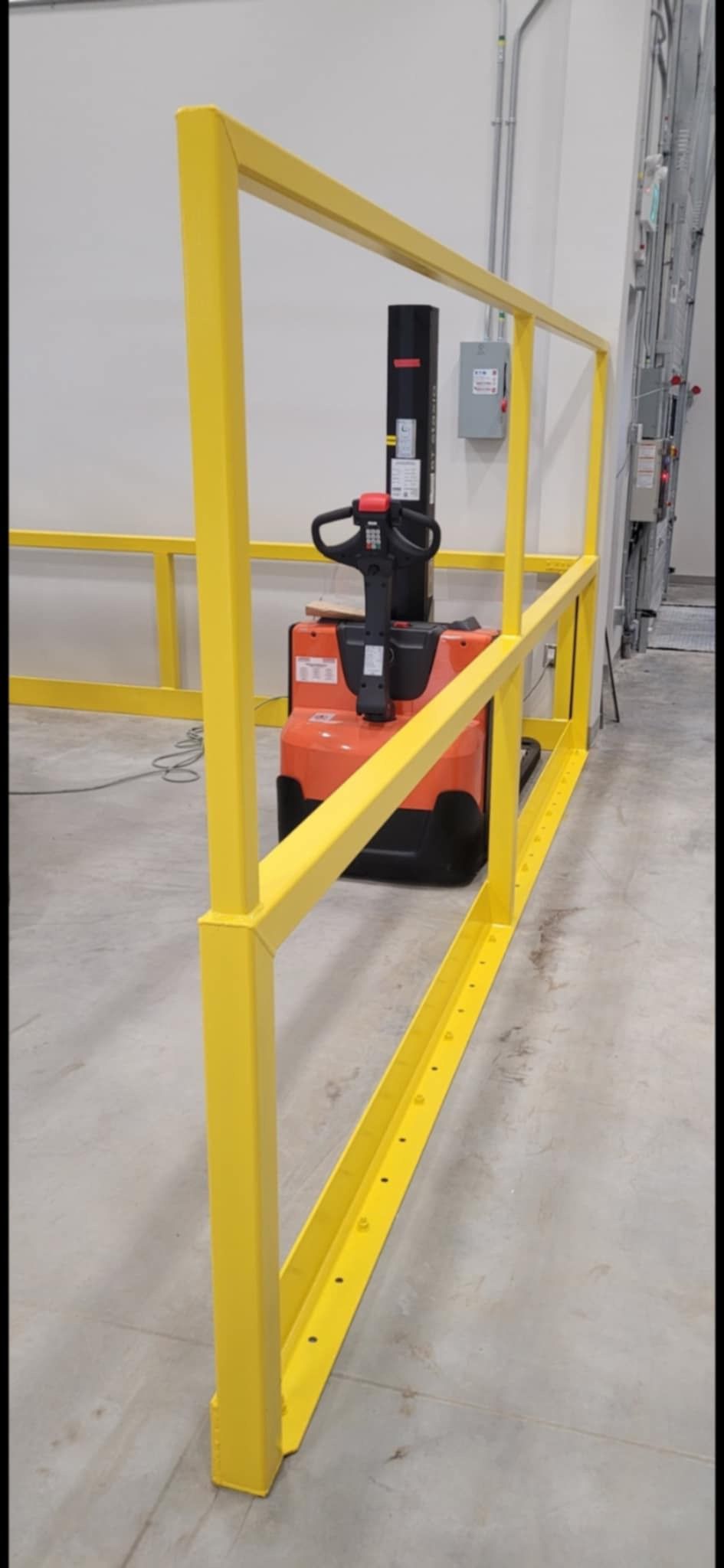 Un chariot élévateur est garé derrière une balustrade jaune dans un entrepôt.