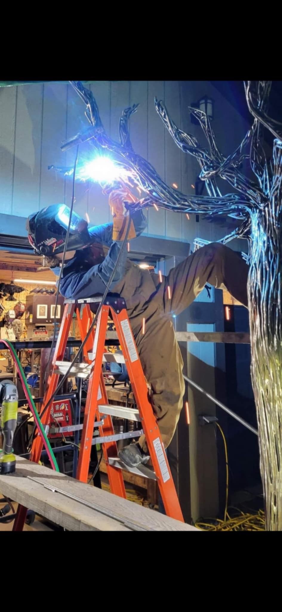Un homme est debout sur une échelle et soude un morceau de métal.