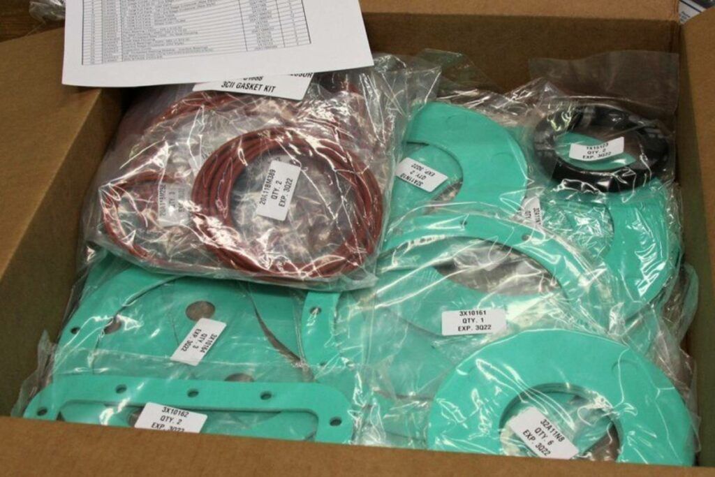 A cardboard box filled with various machine parts, sealed in clear plastic bags.