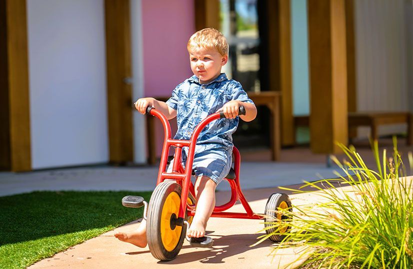 Kindy child outside riding red tricycle with front wheel pedals