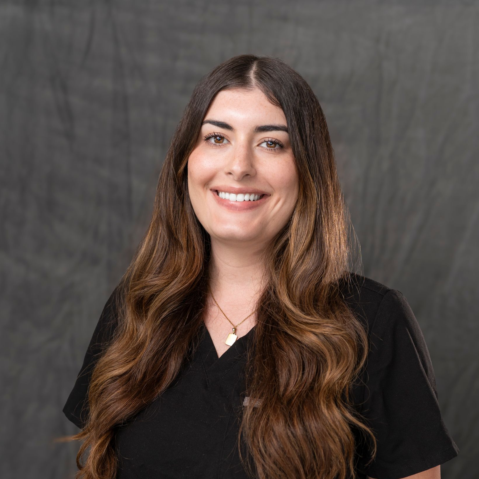 a woman with long blonde hair is wearing a black shirt and a gold necklace .