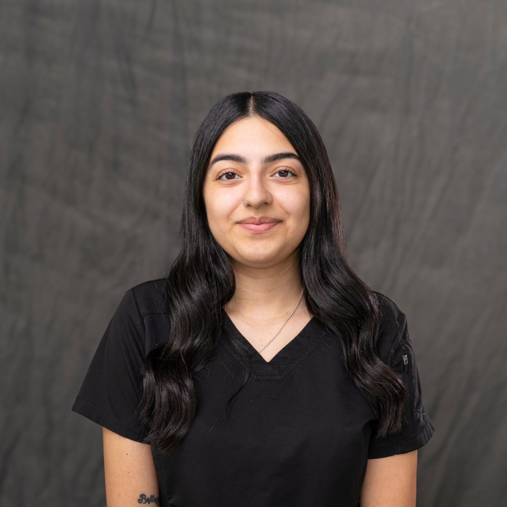 a woman with long hair is wearing a black shirt and standing in front of a white wall .