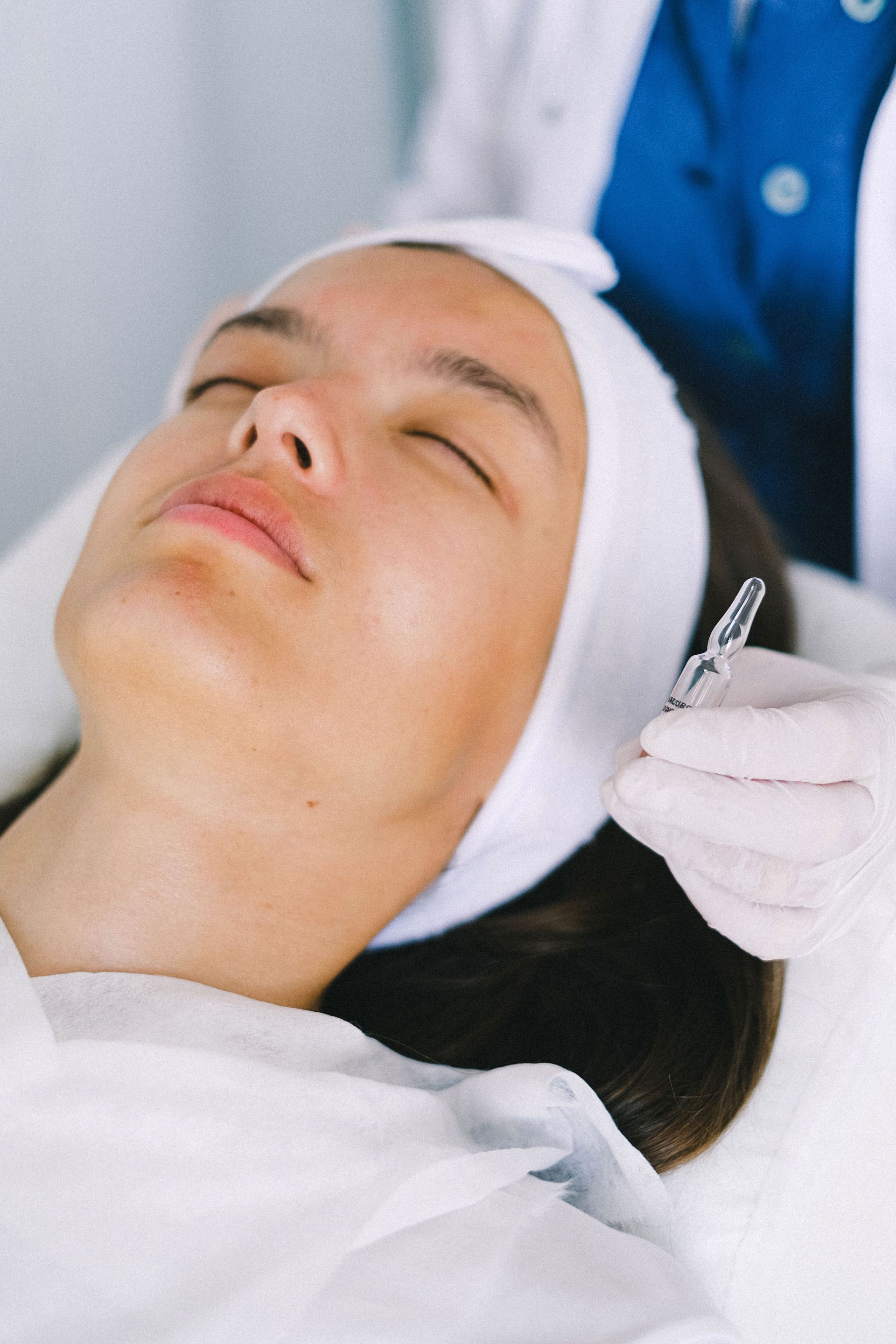 Person lying down while a gloved practitioner holds a small cosmetic tool near the face